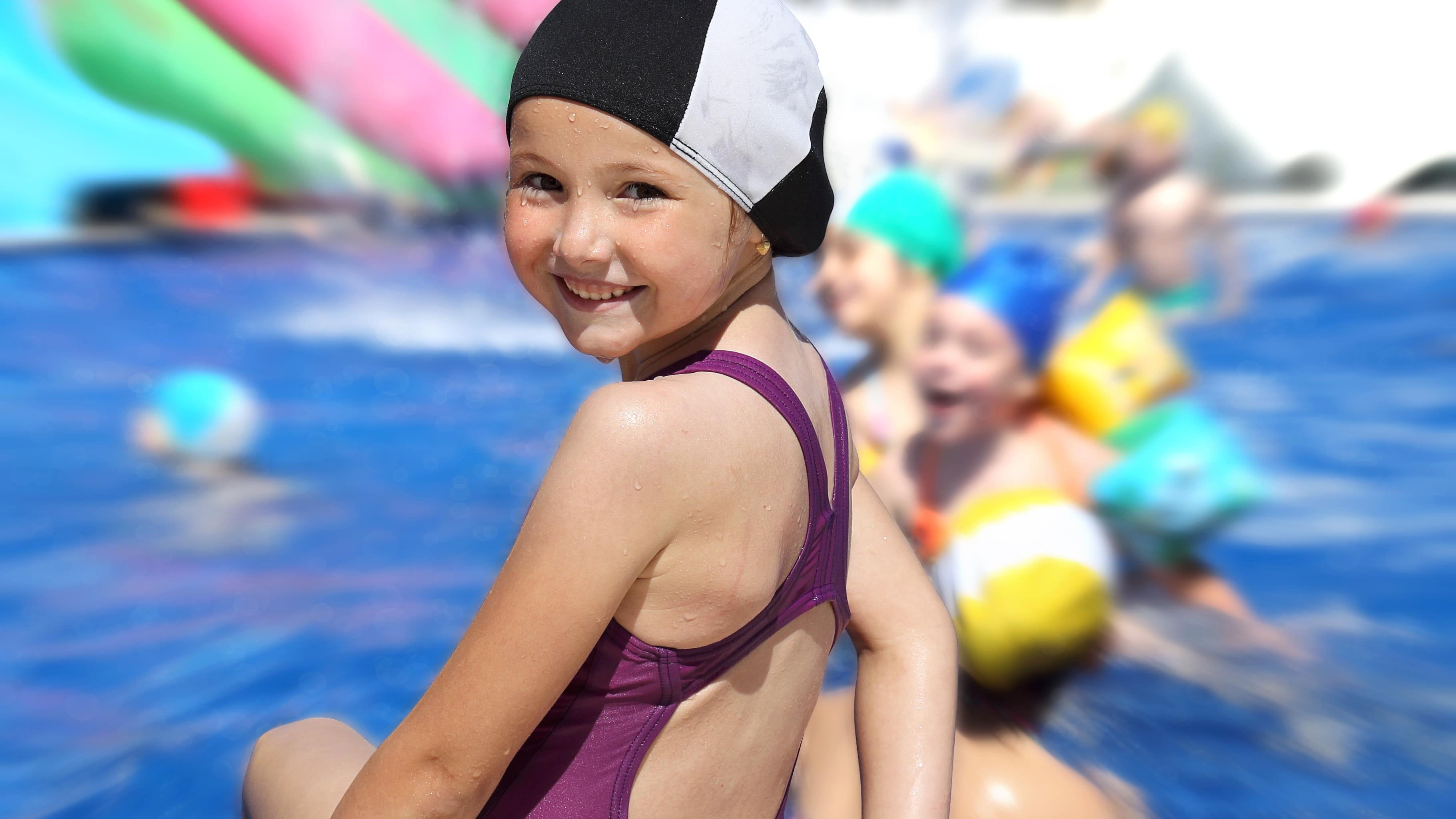 Vue sur des enfants jouant dans une piscine et sur une petite fille portant un bonnet de bain, au premier plan