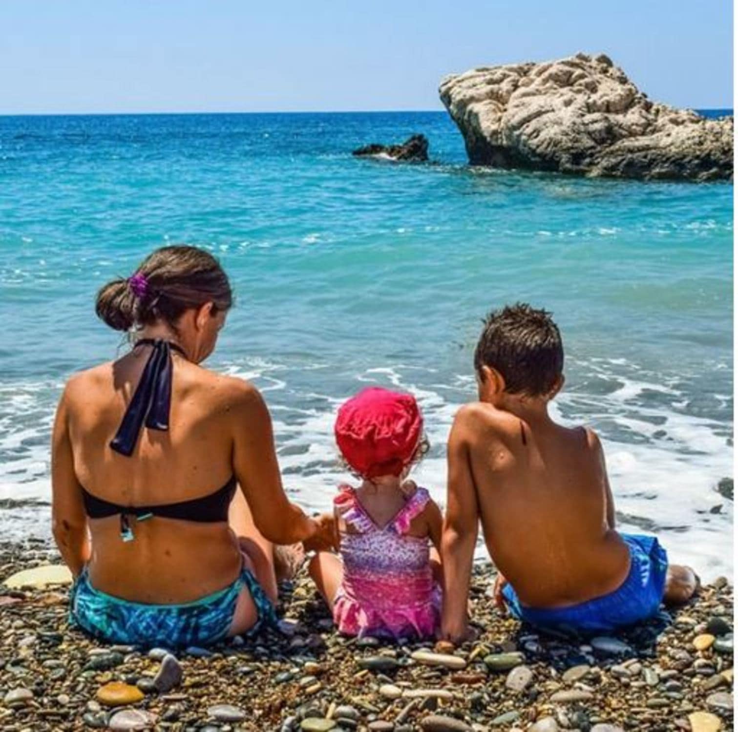 Mère avec ses enfants sur une plage face à la mer, vacances pas cher en famille en aout