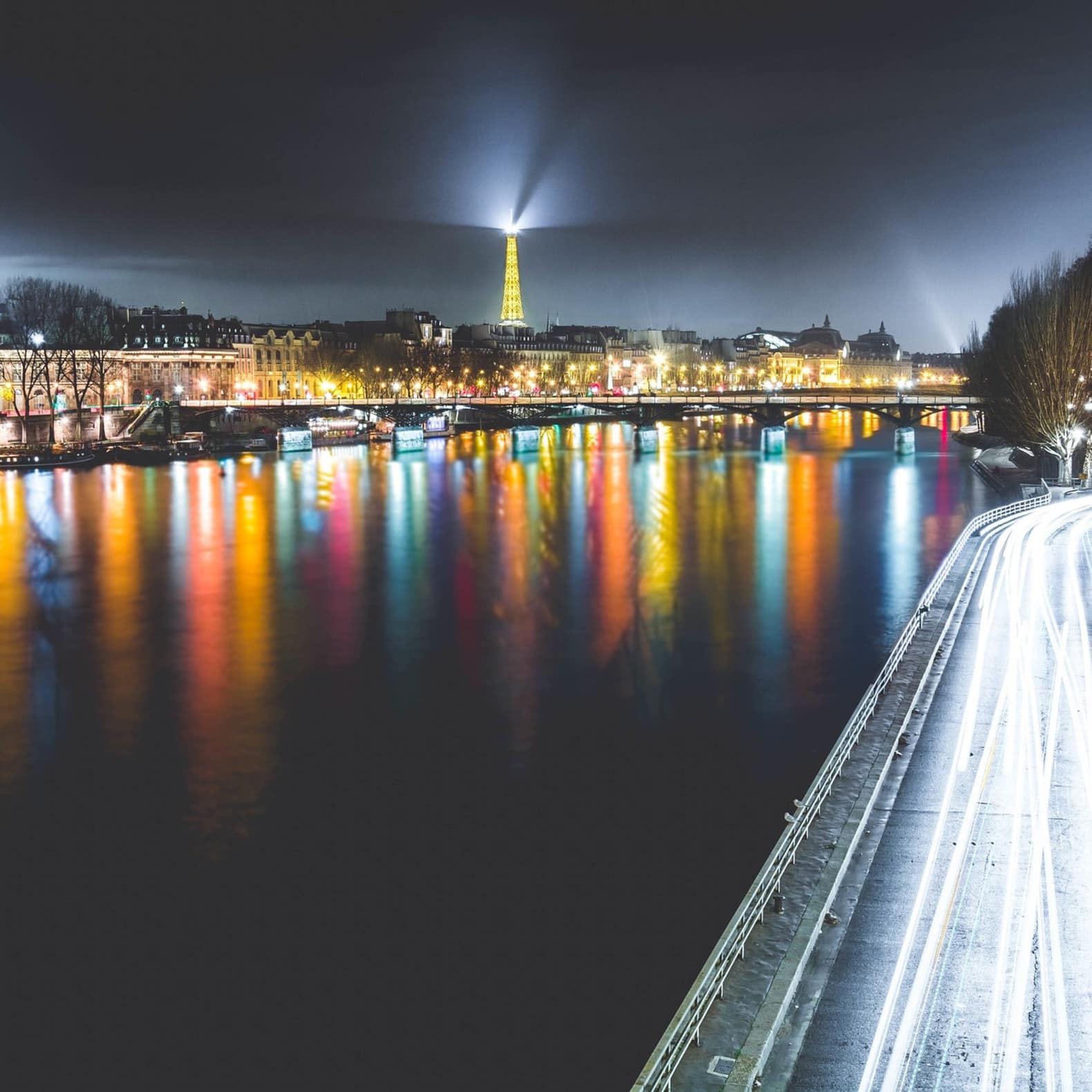Les quais de la Seine de nuit, alors que la tour Eiffel illumine le ciel sombre
