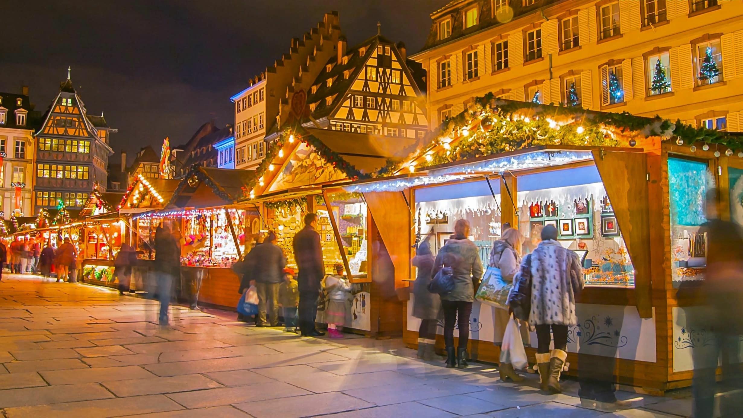 Vue nocturne sur des étals du marché de Noël de Strasbourg, ainsi que sur des promeneurs