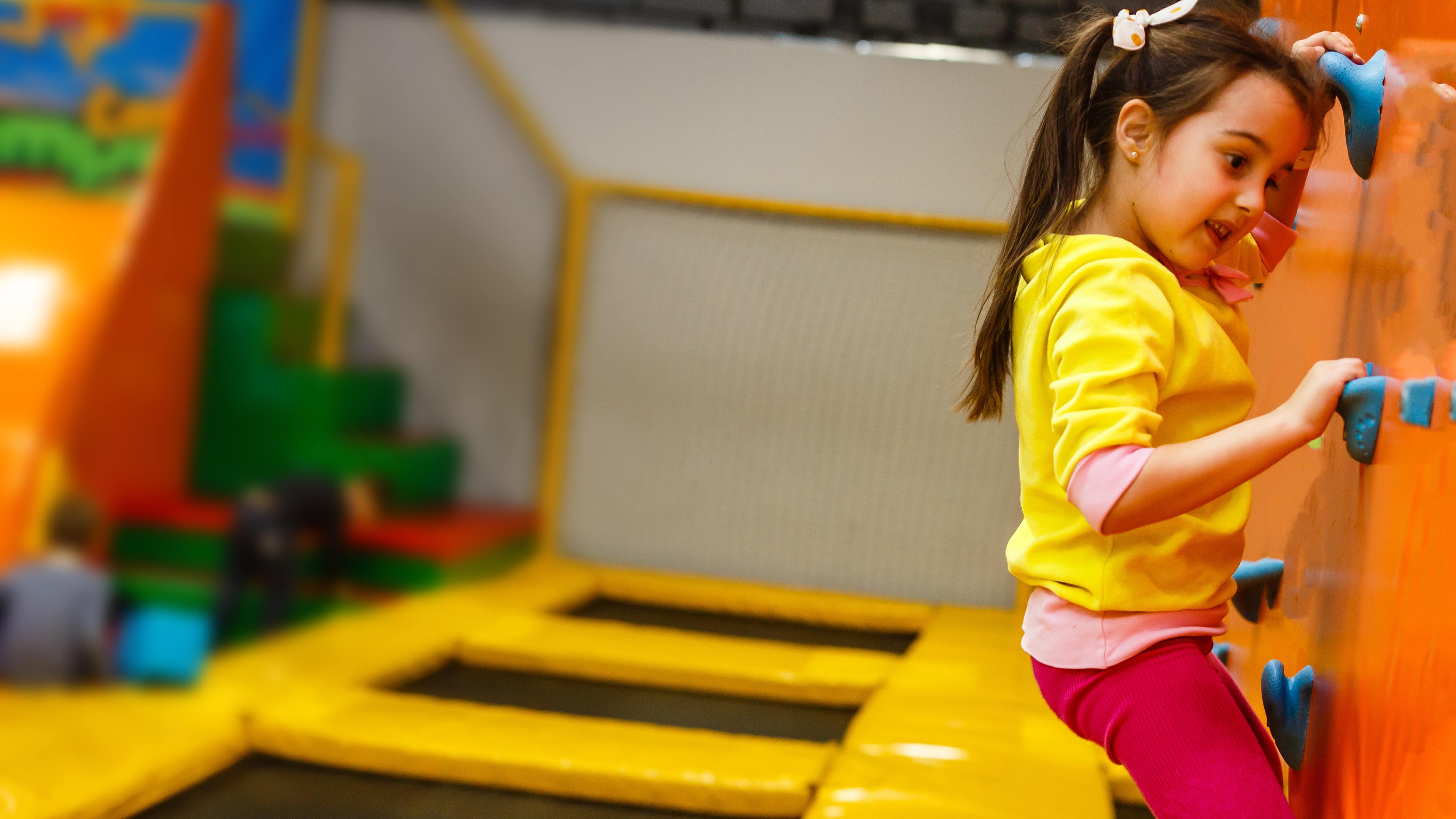 Enfant faisant de l’escalade dans un parc de jeux avec trampolines
