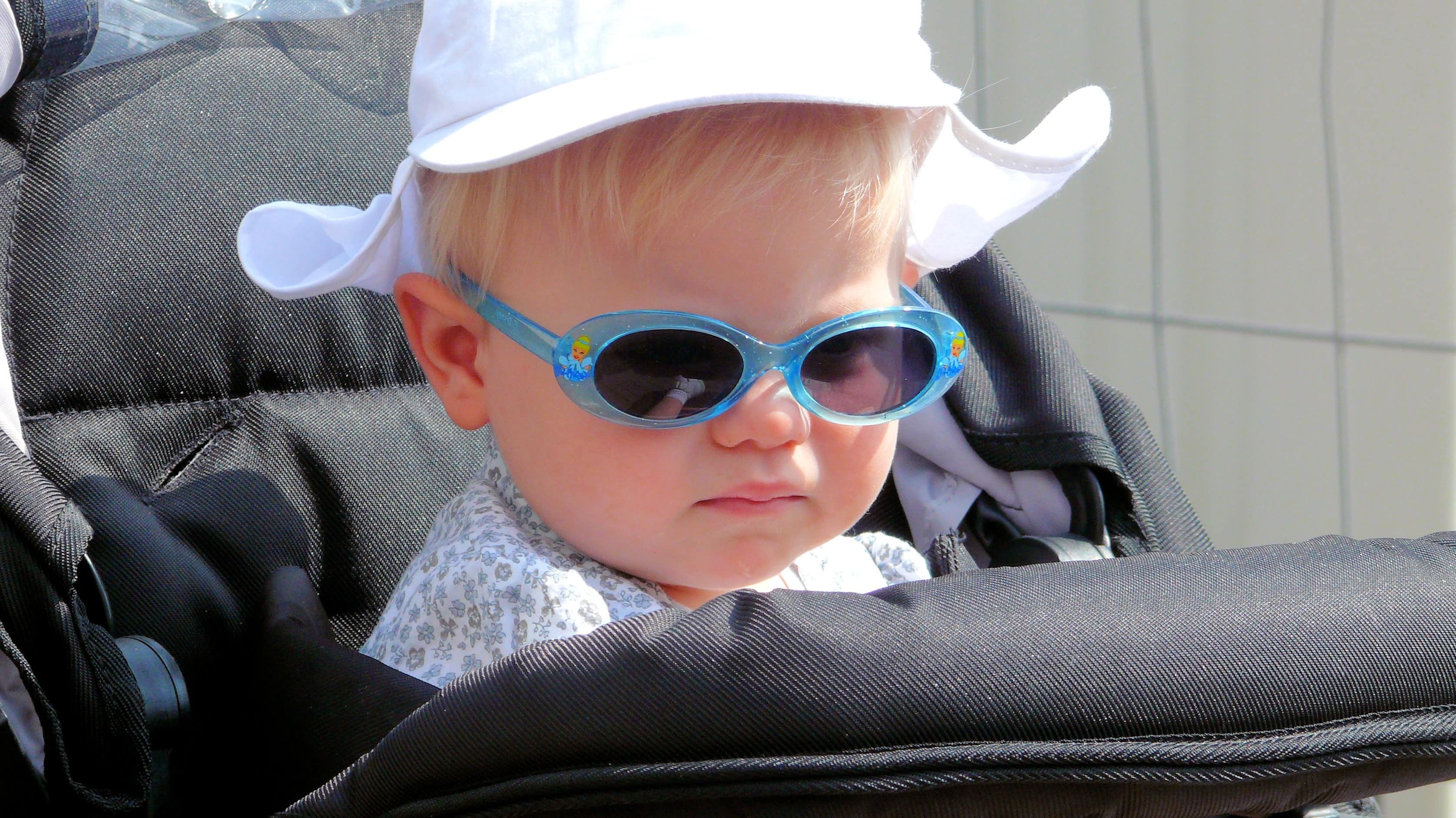 Gros plan sur un bambin dans une poussette, il porte un chapeau et des lunettes de soleil