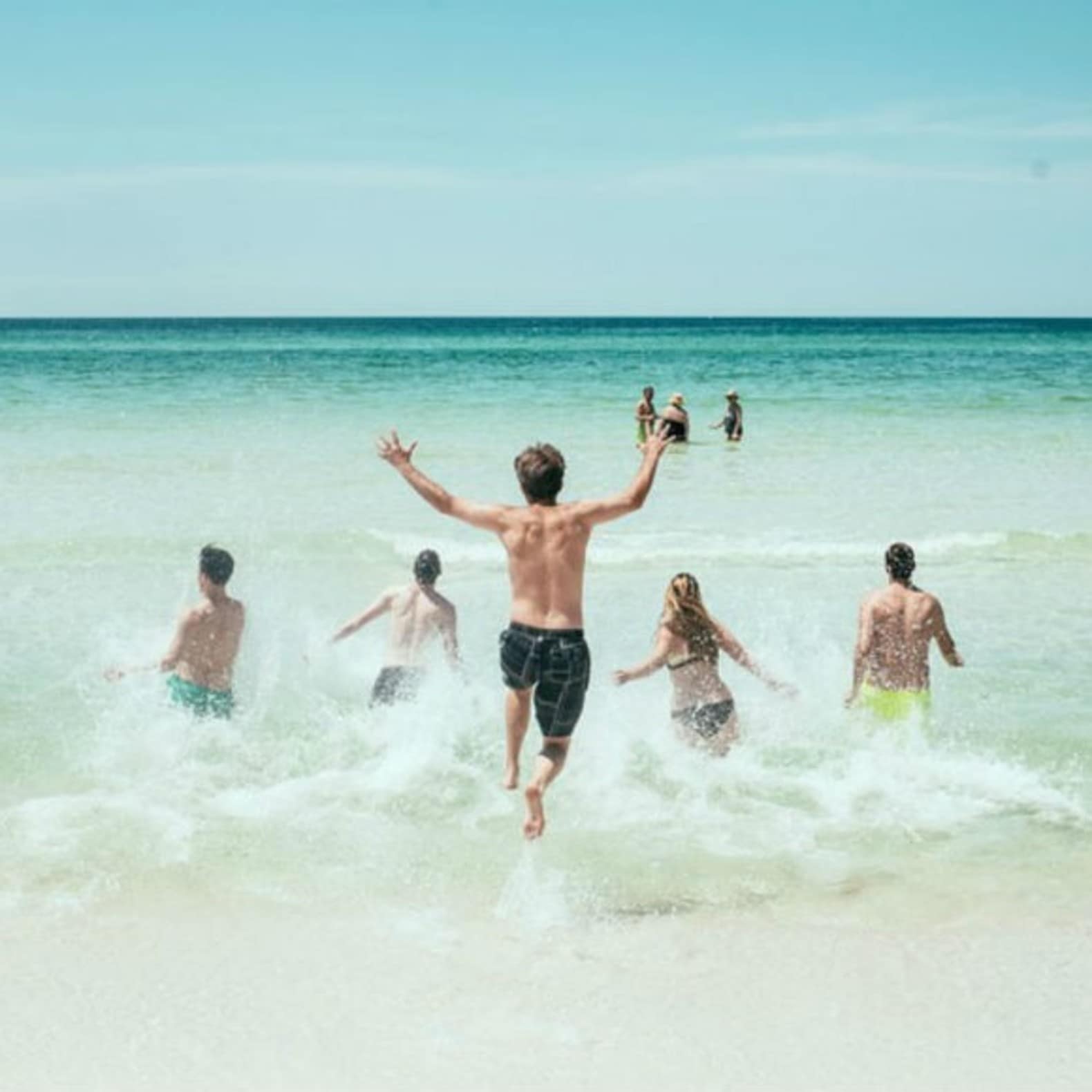 Groupe de personnes courant dans l’eau sur la plage, vacances en famille
