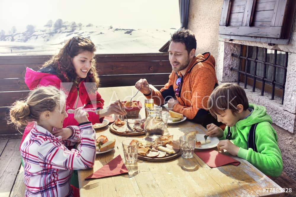 famille mangeant dehors sur le pont d'un chalet entouré de neige