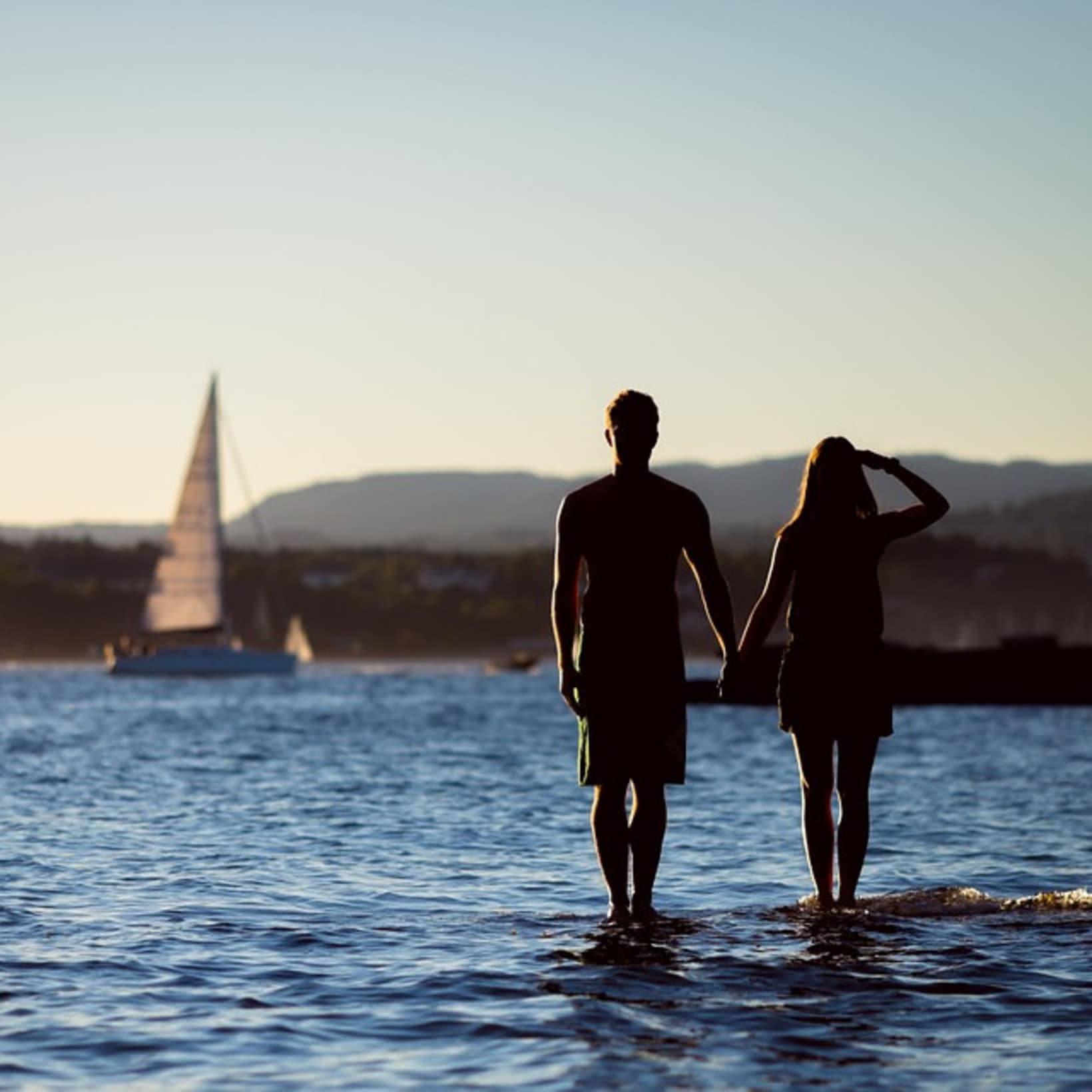 Couple main dans main sur la mer, voilier au second plan