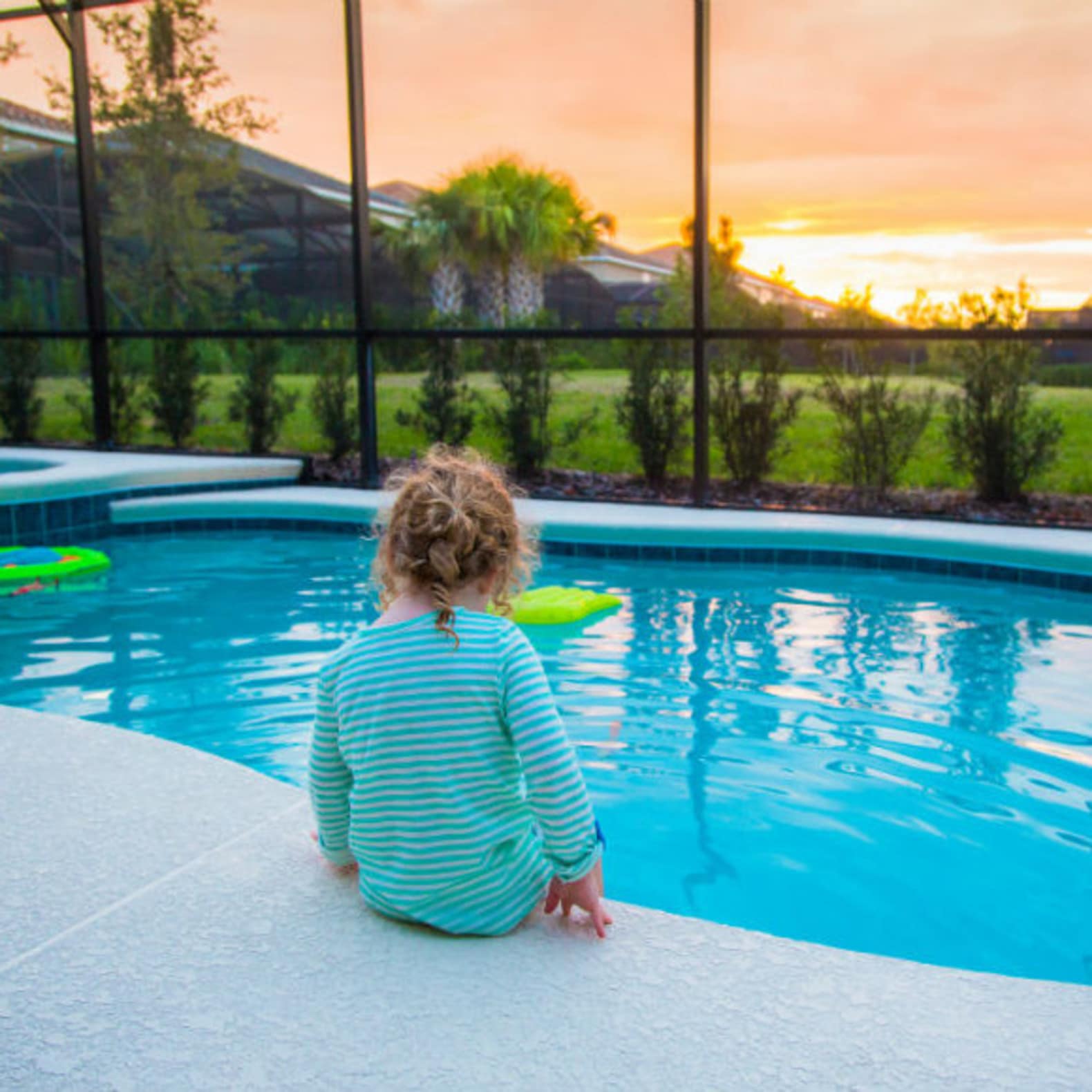 Fillette assise au bord d’une piscine couverte, jardin, soleil couchant, location piscine