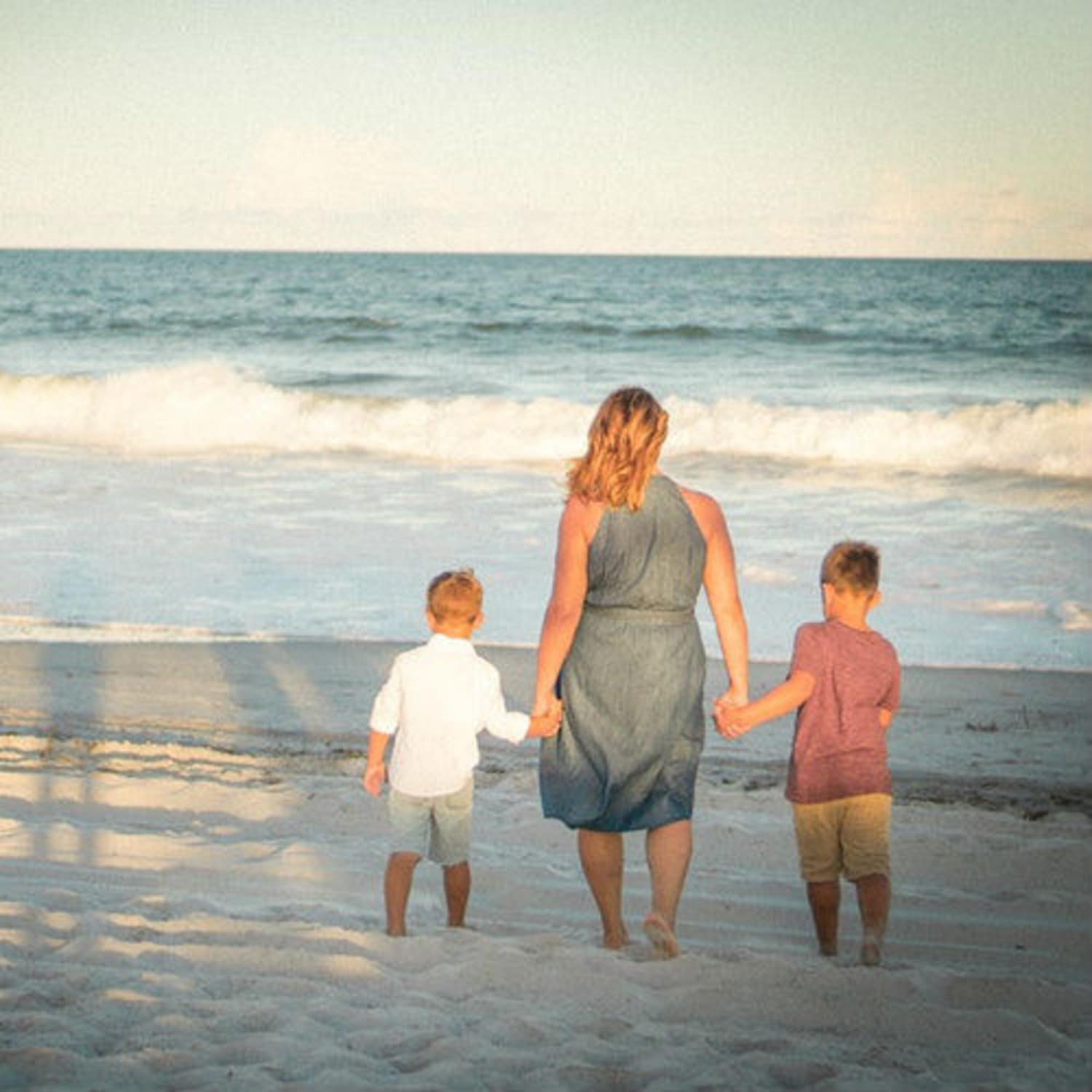 Mère tenant ses enfants par la main sur la plage, face à la mer, location Canet plage