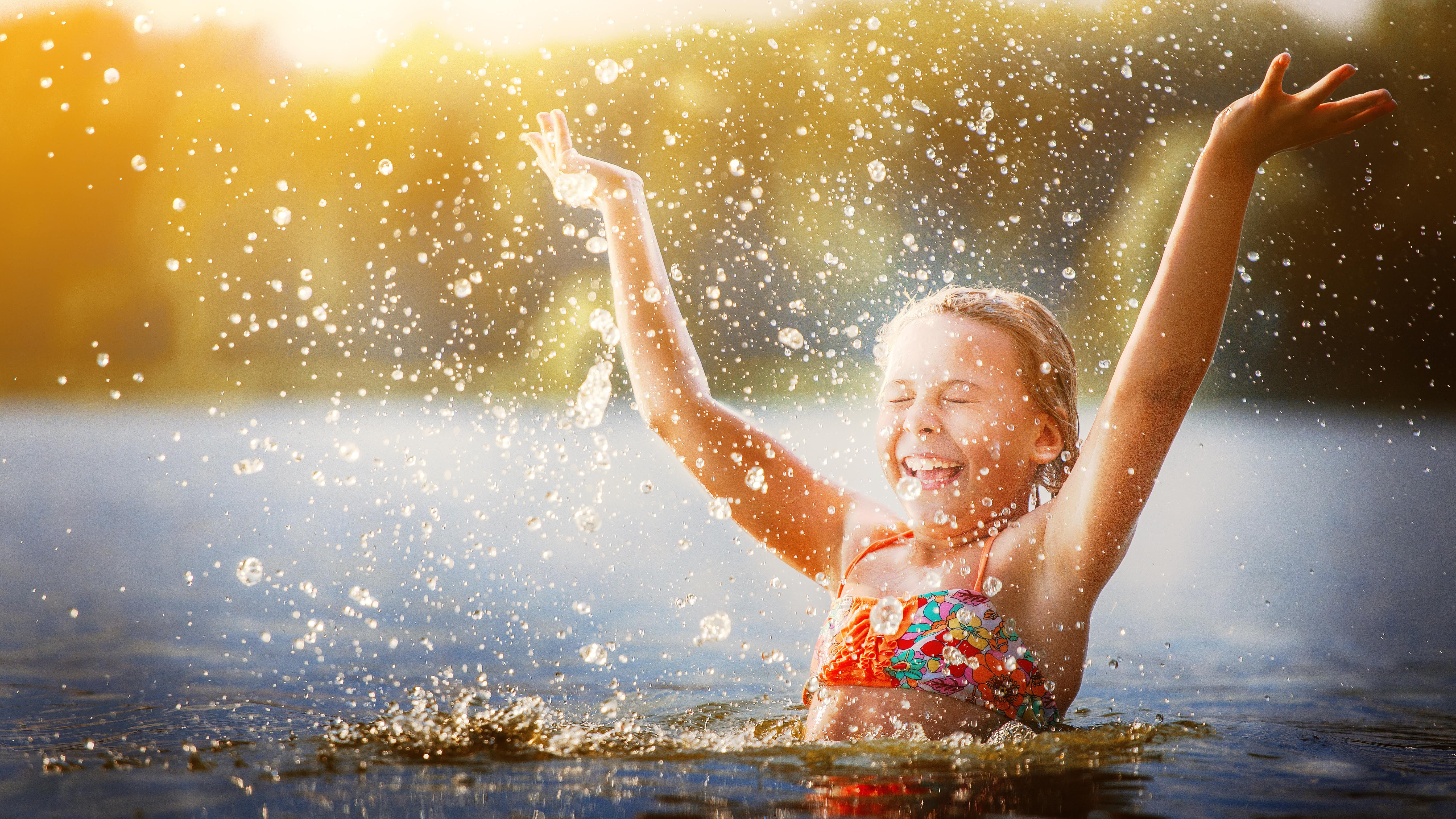 Une petite fille dans l’eau lève les bras en souriant pour s’asperger