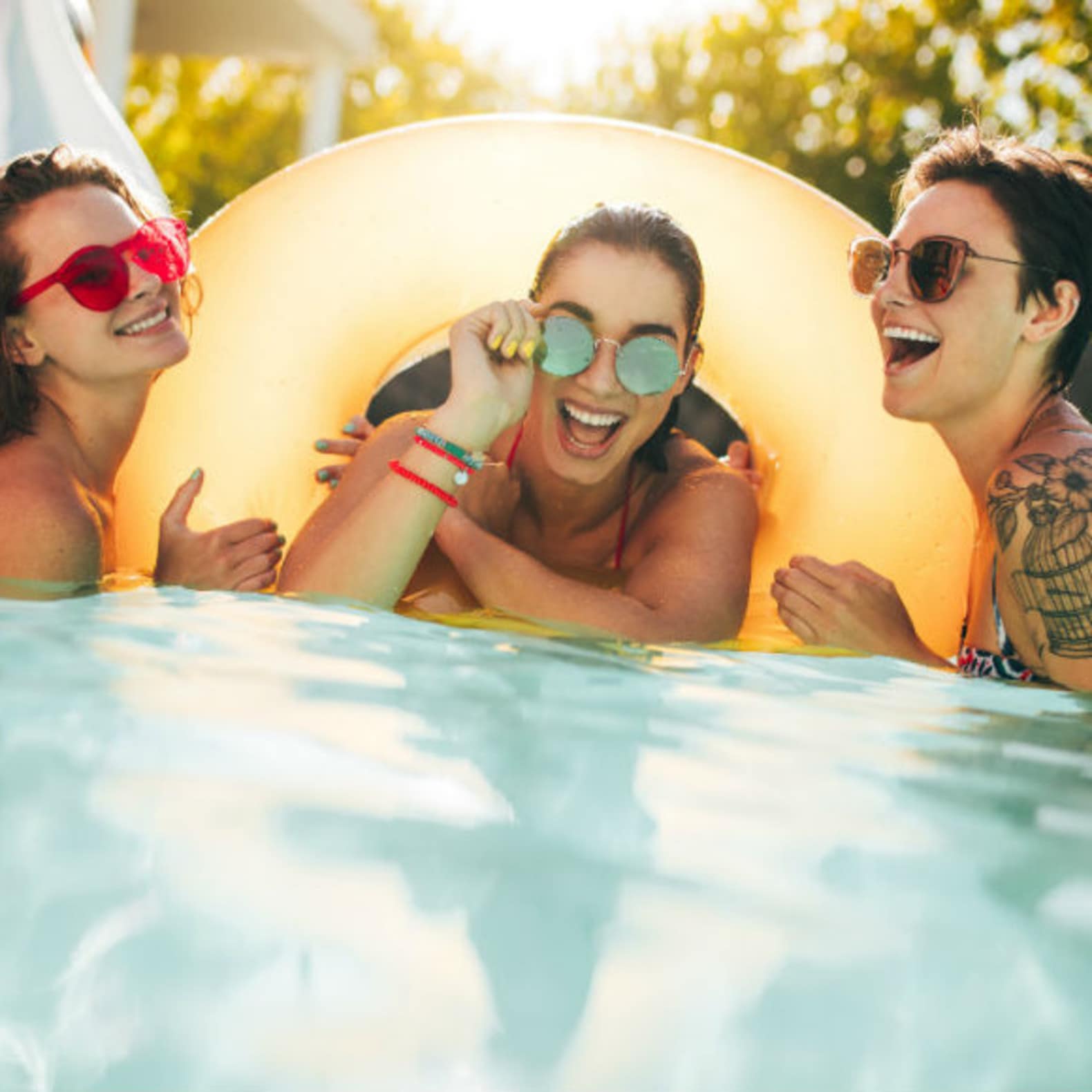 Groupe d’amies avec des lunettes de soleil sur une bouée dans une piscine, location maison avec piscine privée