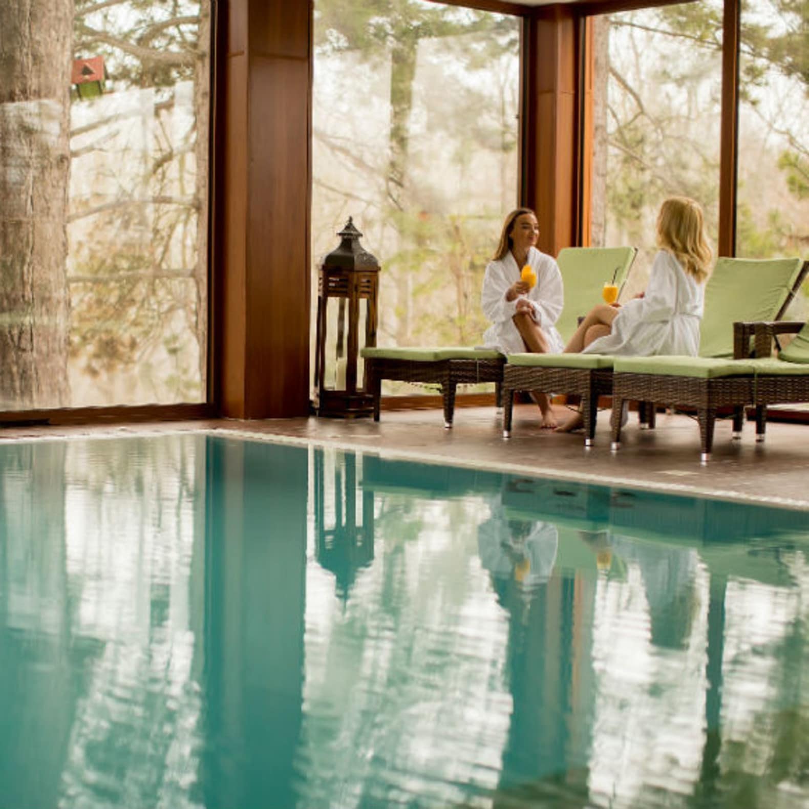 Deux femmes en peignoir buvant un verre au bord d’une piscine intérieure, location maison avec piscine
