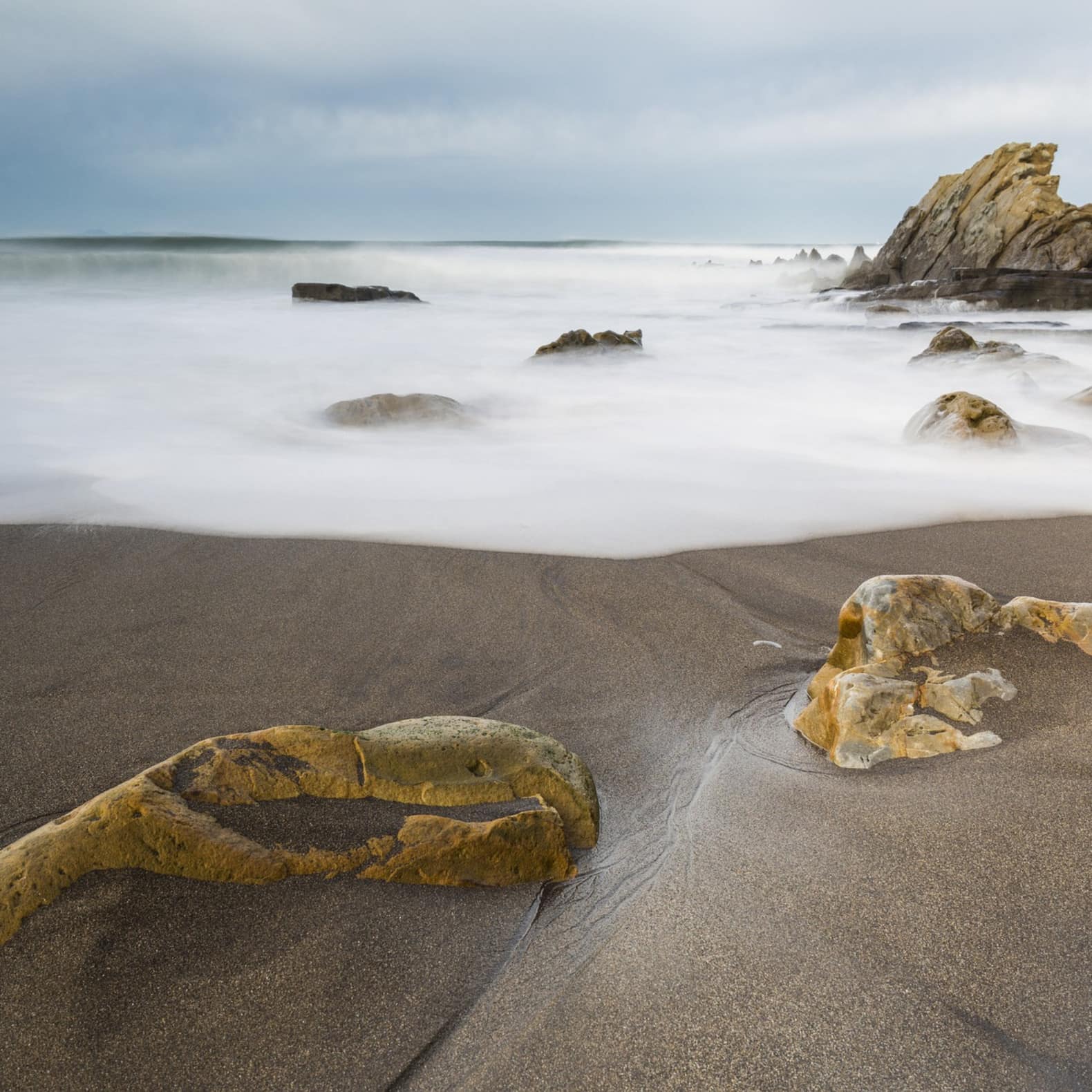 Plage de sable gris, avec des rochers ocre, au bord de l'océan atlantique. Beauté sauvage du Pays basque