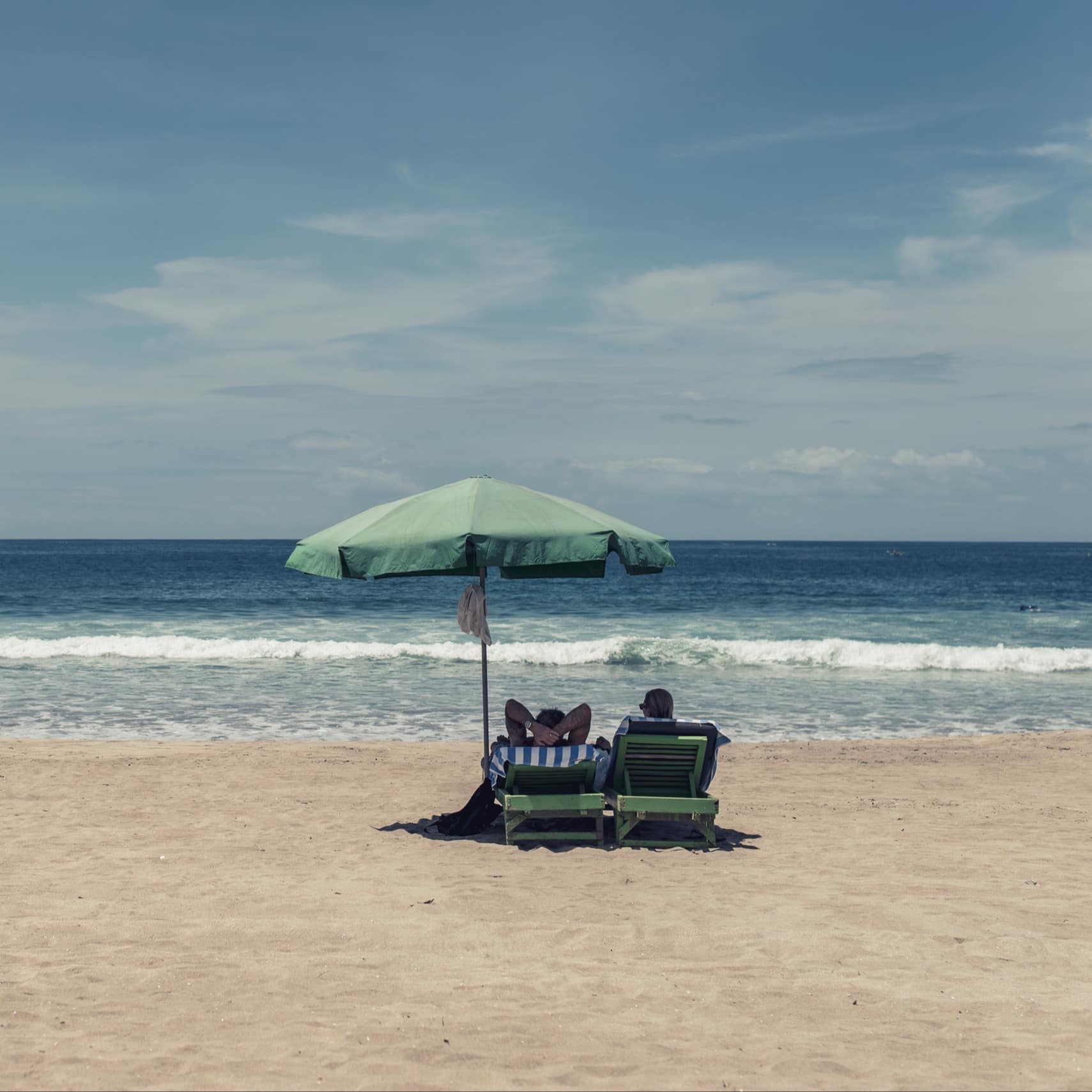 Couple sur des chaises longues sous un parasol sur la plage, face à la mer, location vacances Normandie bord de mer