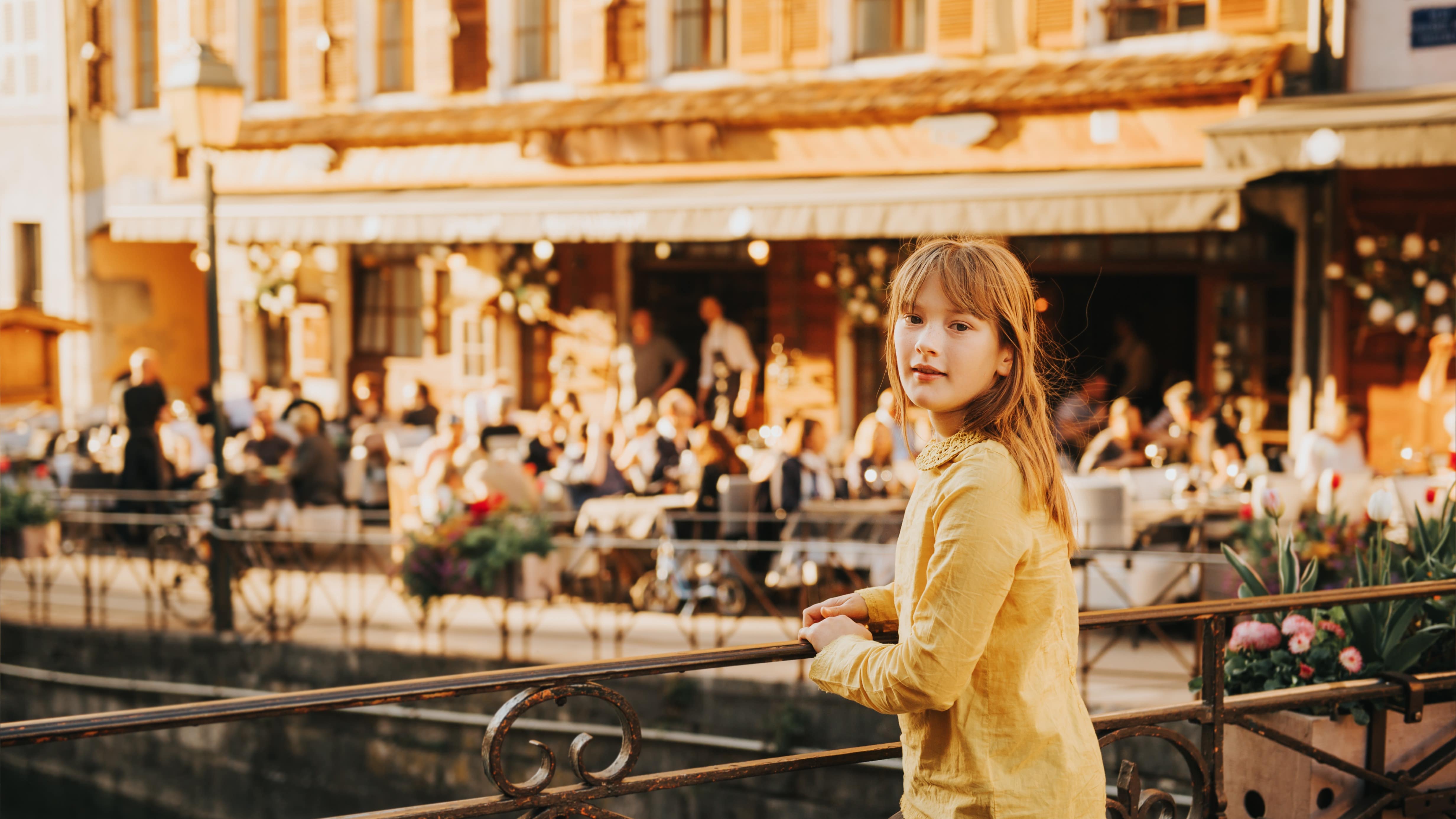 Une jeune fille sur un pont enjambant un canal bordé par les terrasses d’un restaurant à Annecy
