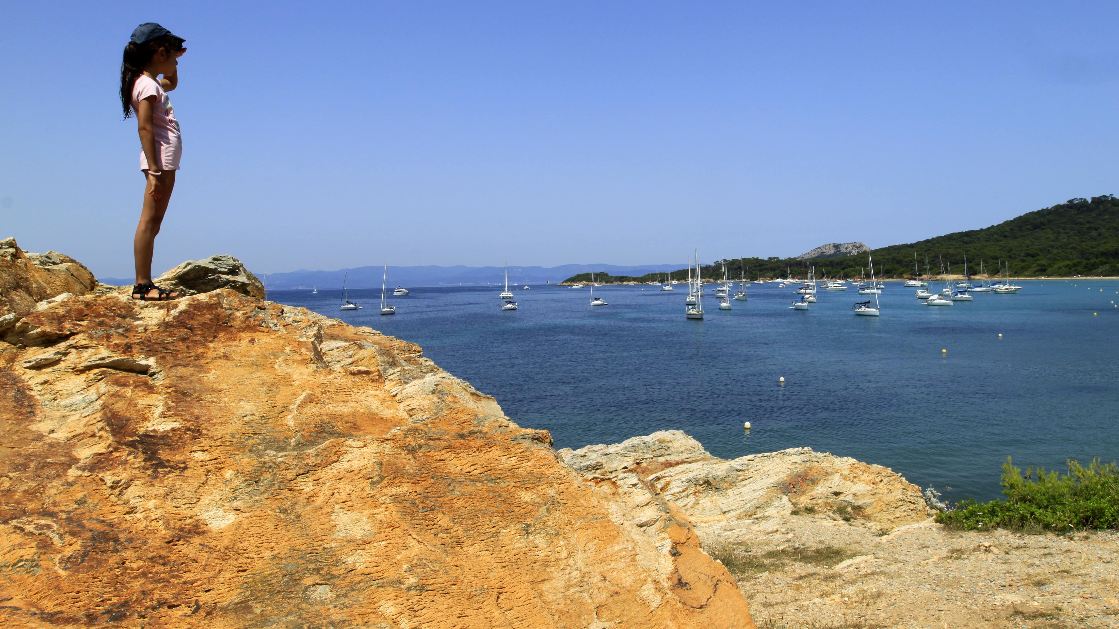 Une enfant perchée sur un rocher admire la baie sur l’île de Porquerolles