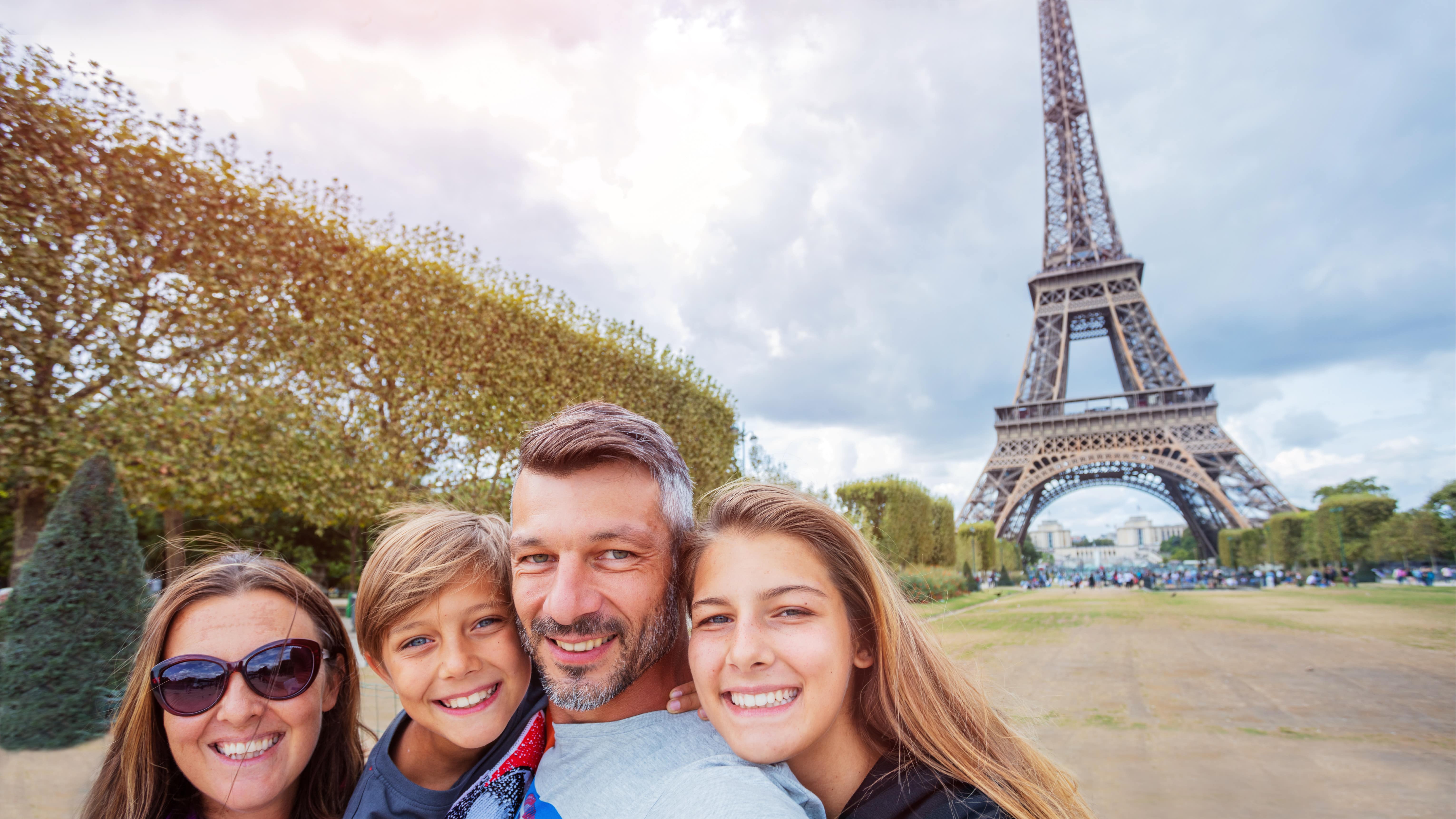 Une famille souriante se prenant en photo devant la tour Eiffel à Paris