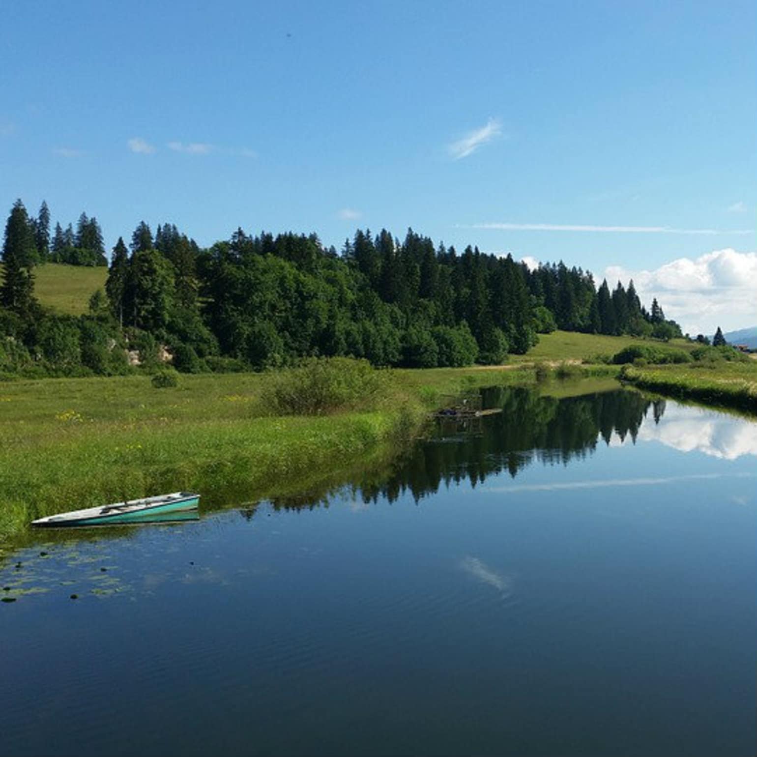 un bateau amarré sur un lac dans un paysage de montagne et de forêt verdoyante du Jura en France