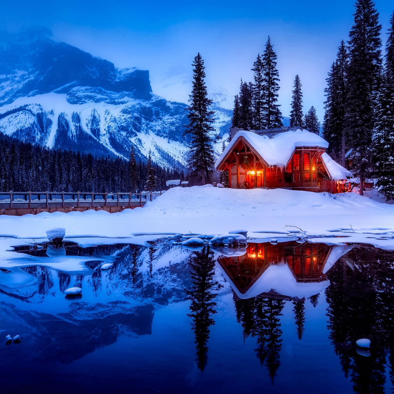 Petit chalet éclairé au crépuscule au bord d’un lac et de montagnes au Canada