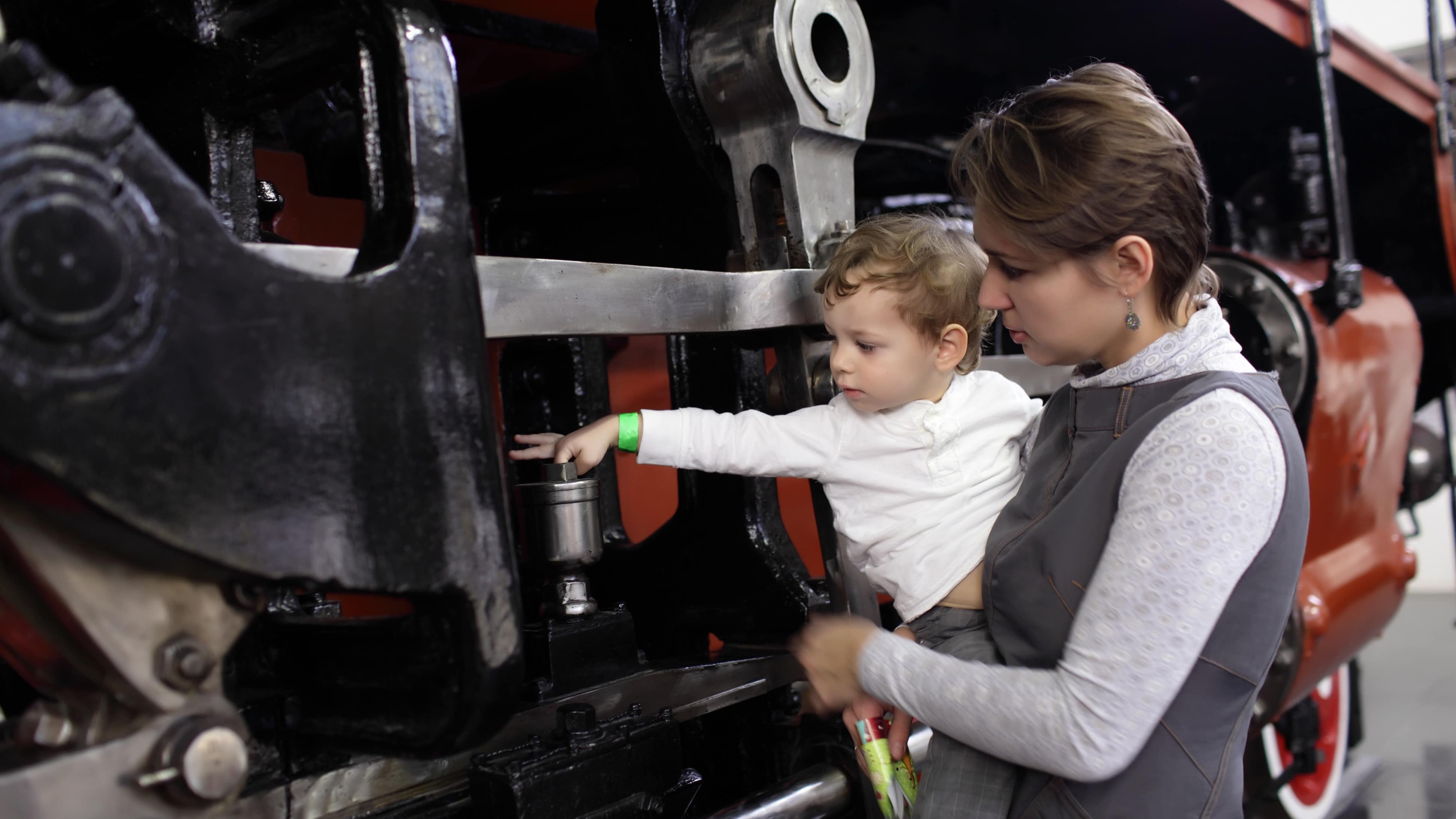 Un enfant, dans les bras de sa mère, touche une locomotive ancienne