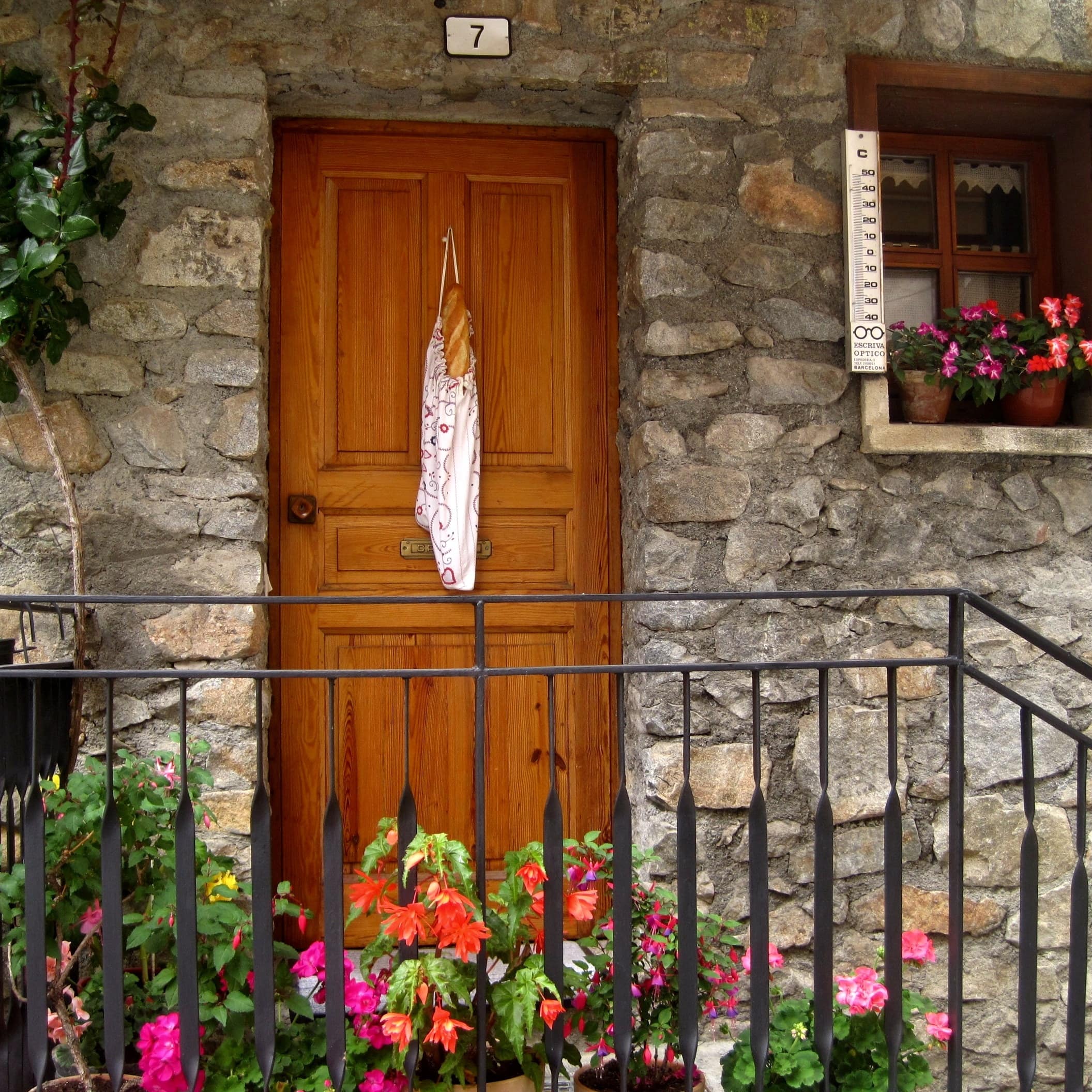 La façade d’un chalet en pierres, bordée de fleurs rouges