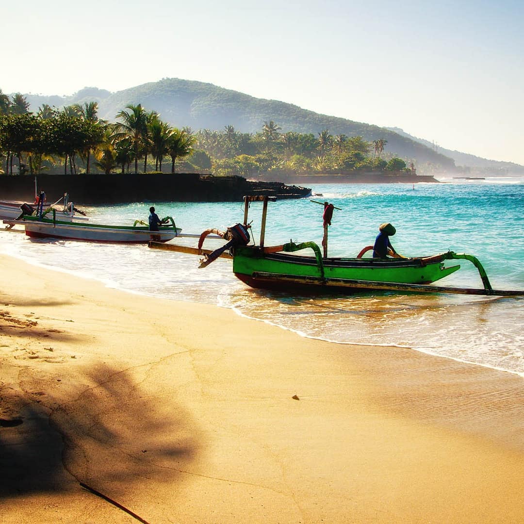 Traditional Balinese fishing boats, jukungs, on a Seminyak beach with golden sands, aquamarine water and palm trees