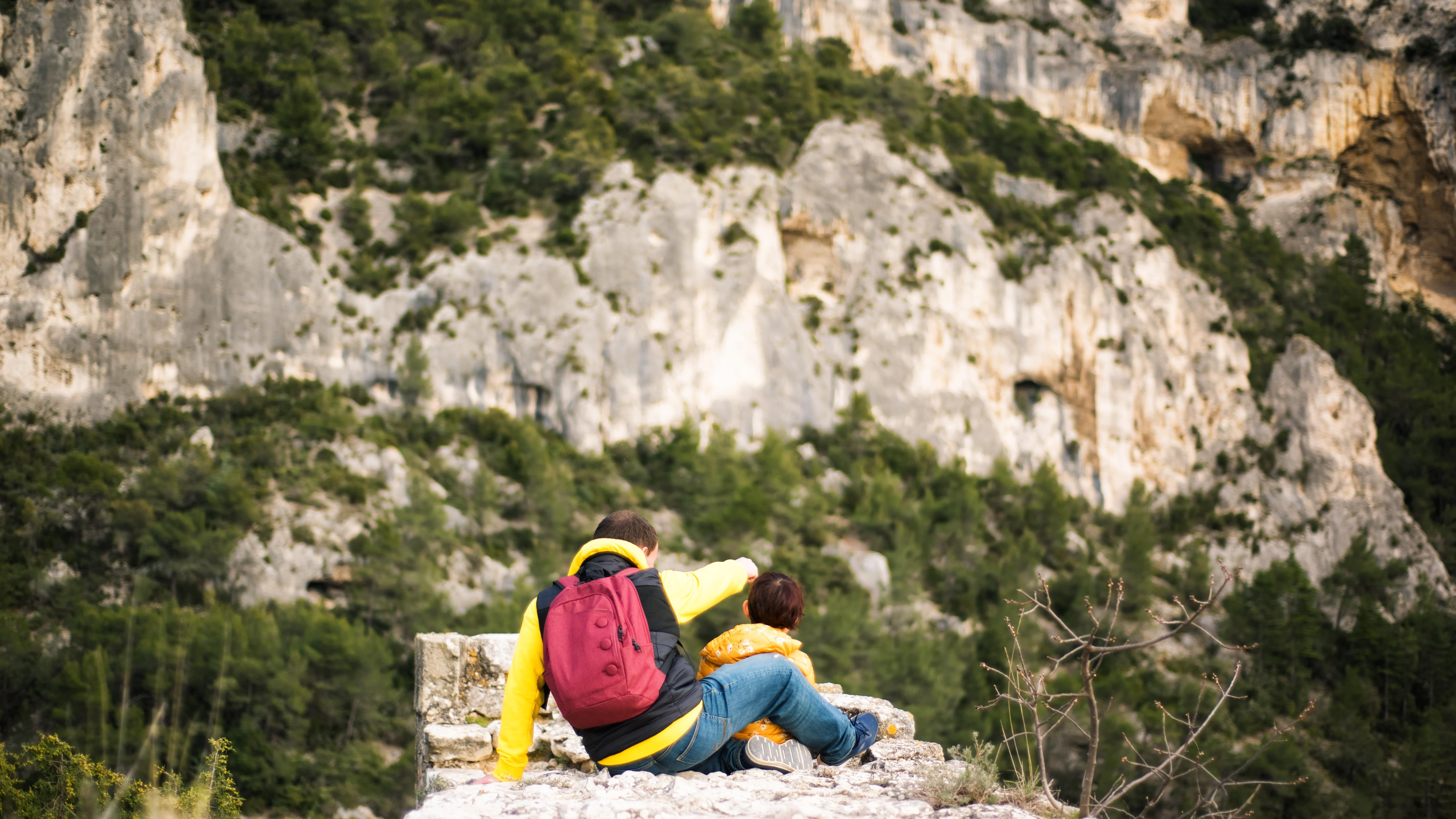 Un père et son fils assis sur un promontoire rocheux face aux falaises calcaires du Parc naturel du Luberon