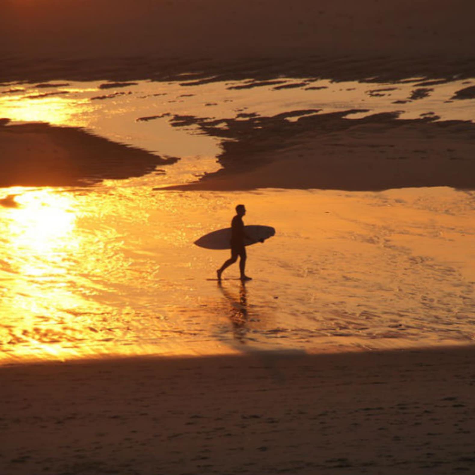Homme sur la plage avec une planche de surf, soleil couchant, location Mimizan plage