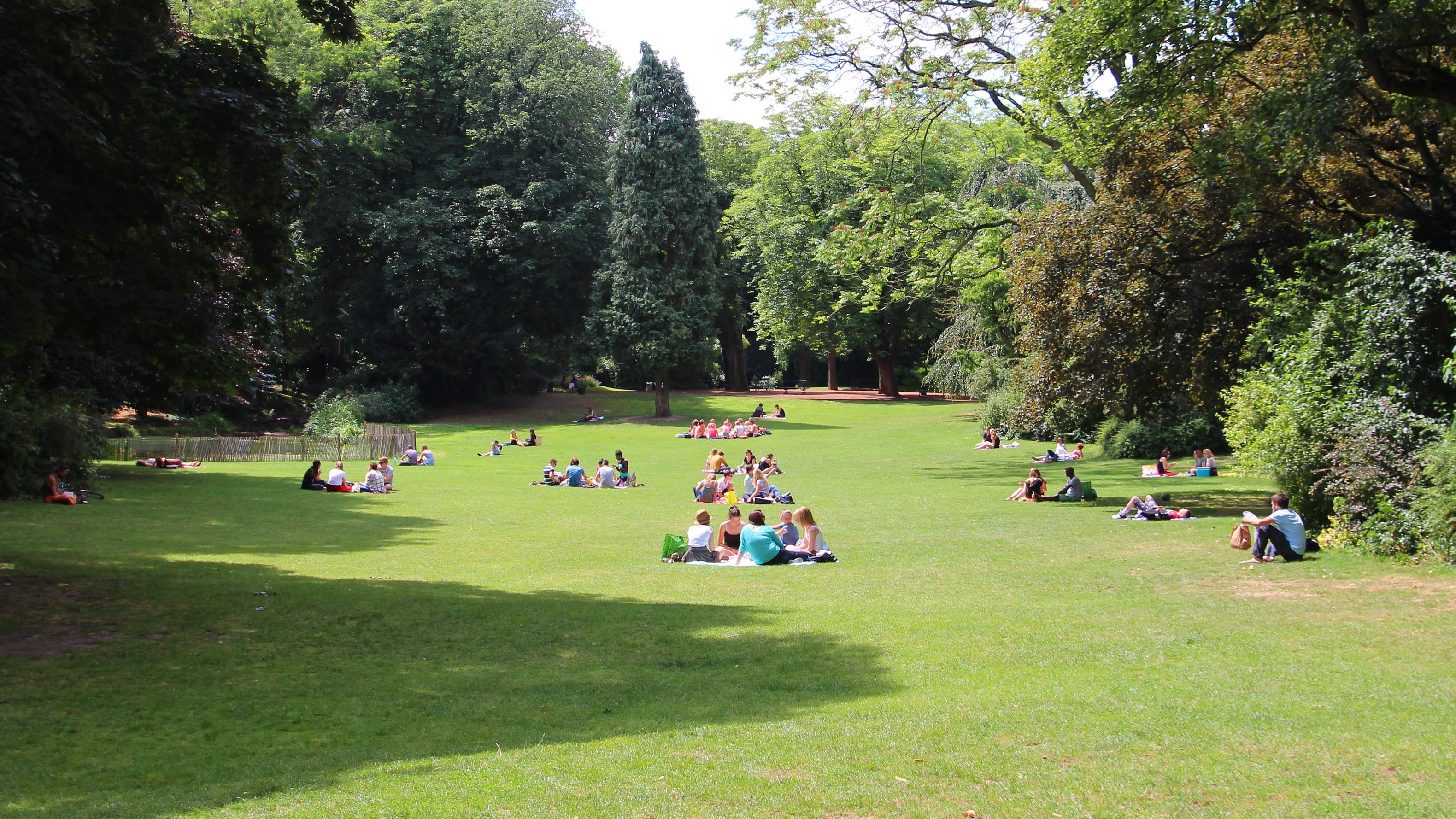 Vue sur une étendue verte du parc de la Citadelle et sur plusieurs groupes de personnes assises dans l'herbe