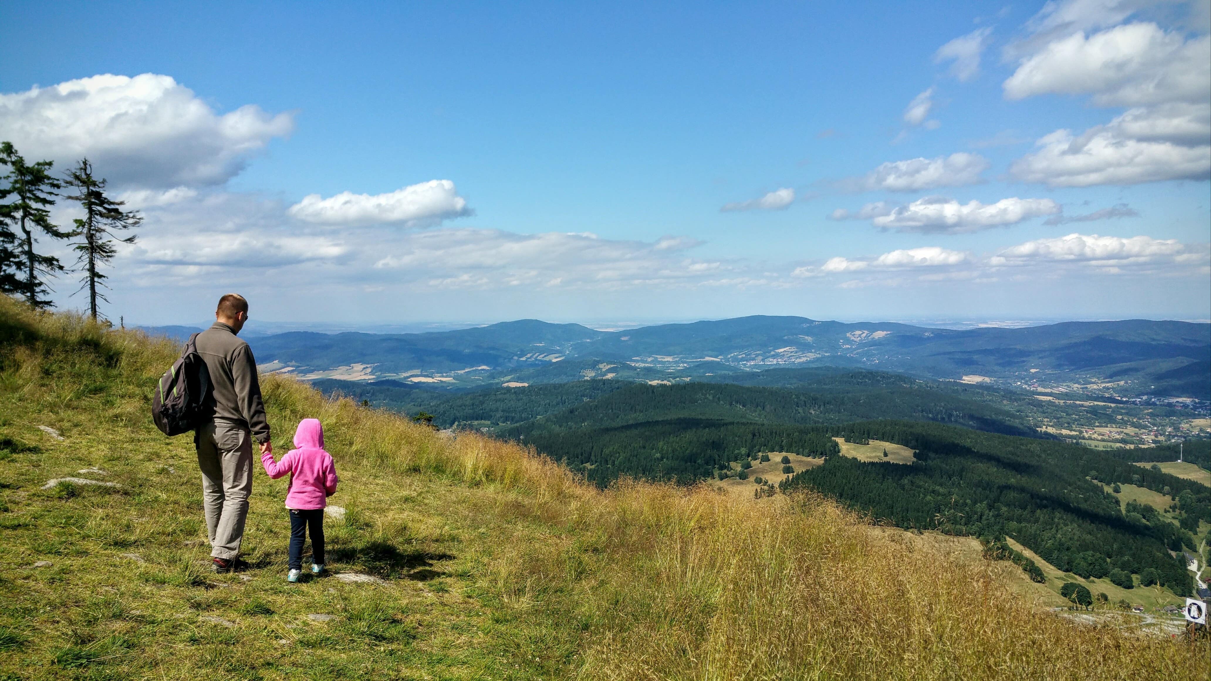Un papa et sa petite fille admirant un panorama de montagnes sous un ciel bleu voilé de quelques nuages