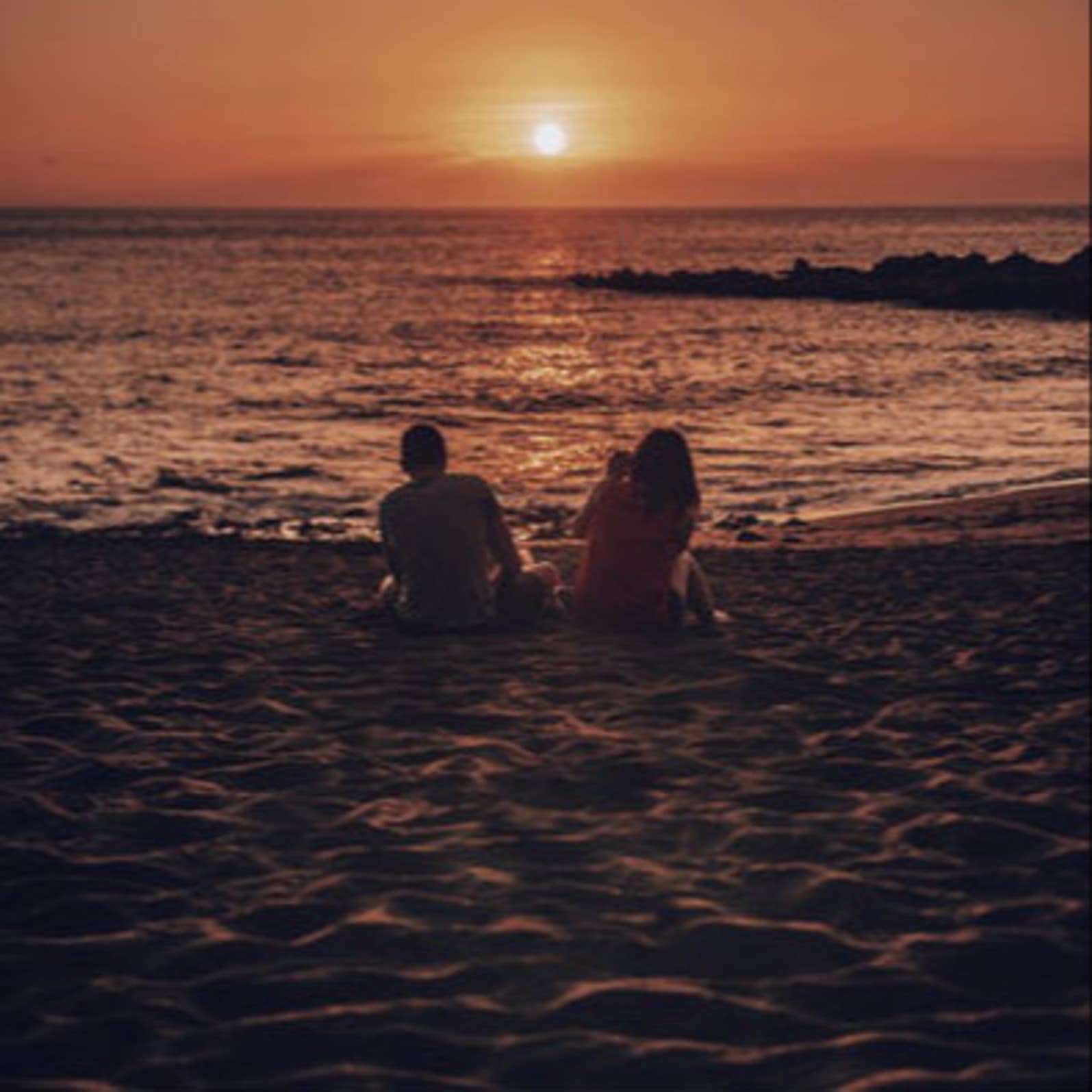 Couple assis sur le sable d’une plage, face au soleil couchant, coucher de soleil, location Canet plage