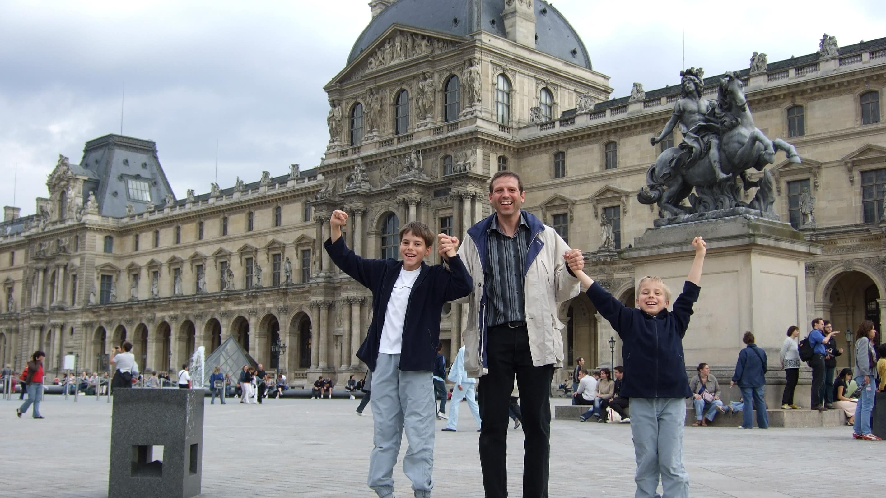 Un père tenant ses deux garçons par la main sur l’esplanade du musée du Louvre à Paris