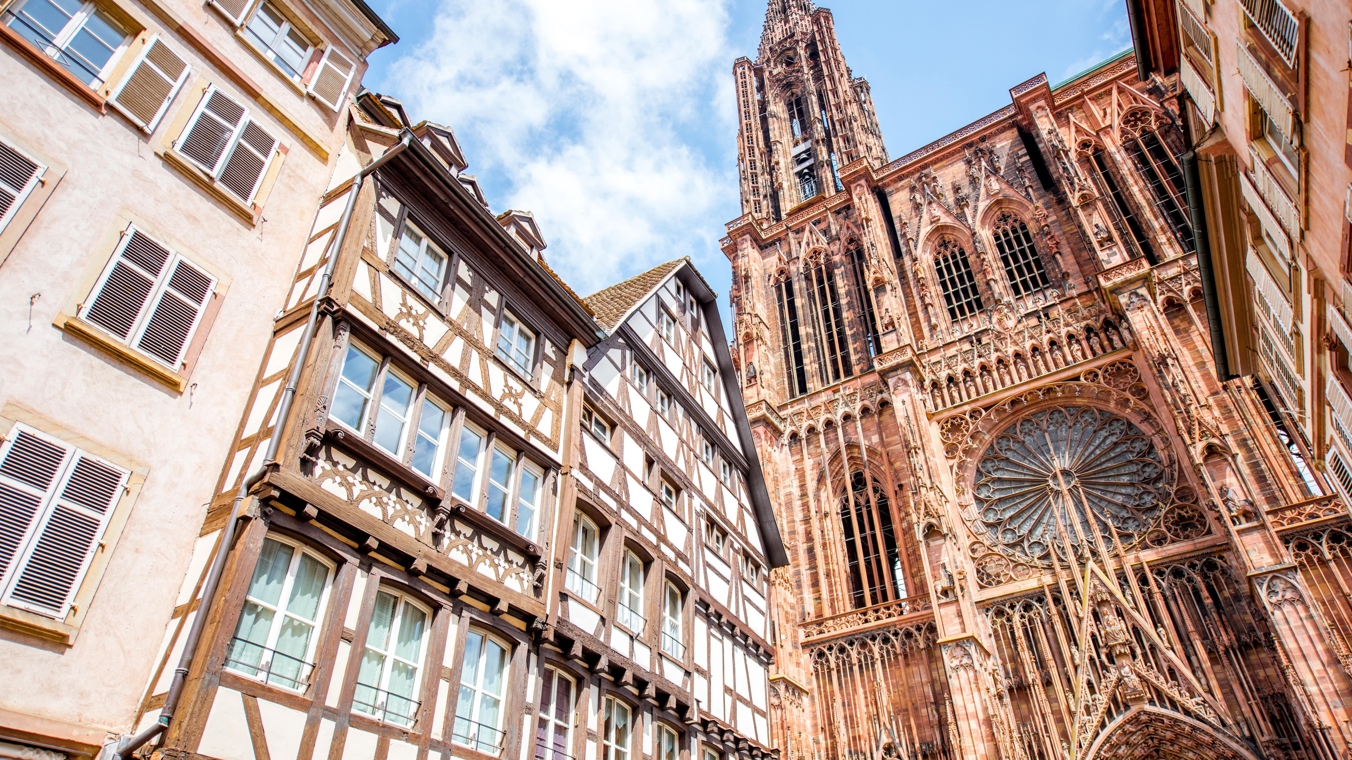 Vue d'en bas sur une maison à colombages, à gauche, ainsi que la cathédrale de Strasbourg, à droite