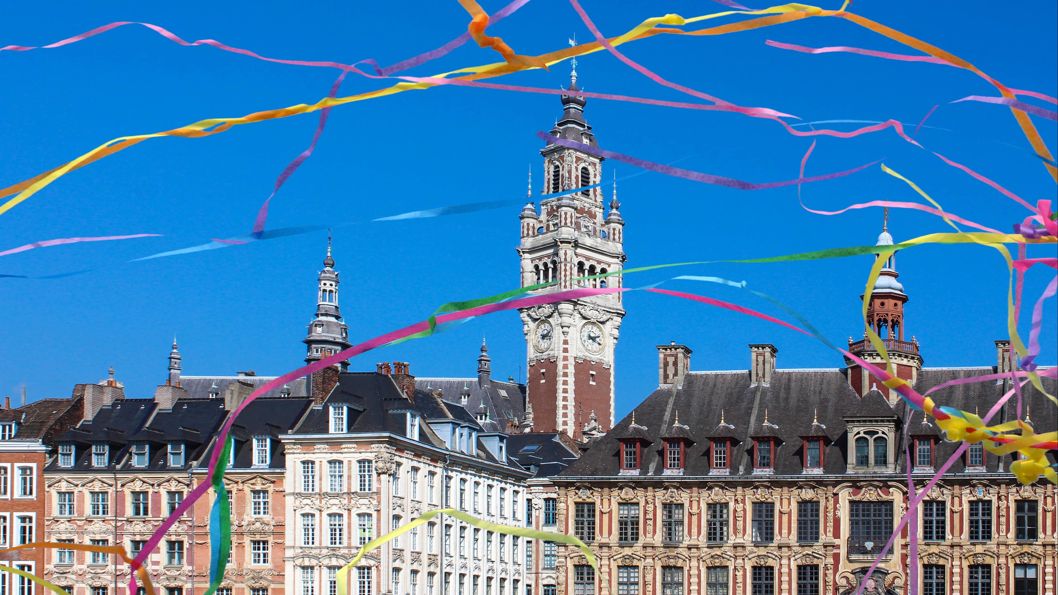 Vue sur le beffroi de Lille, sur fond de ciel bleu, des serpentins colorés volant au premier plan