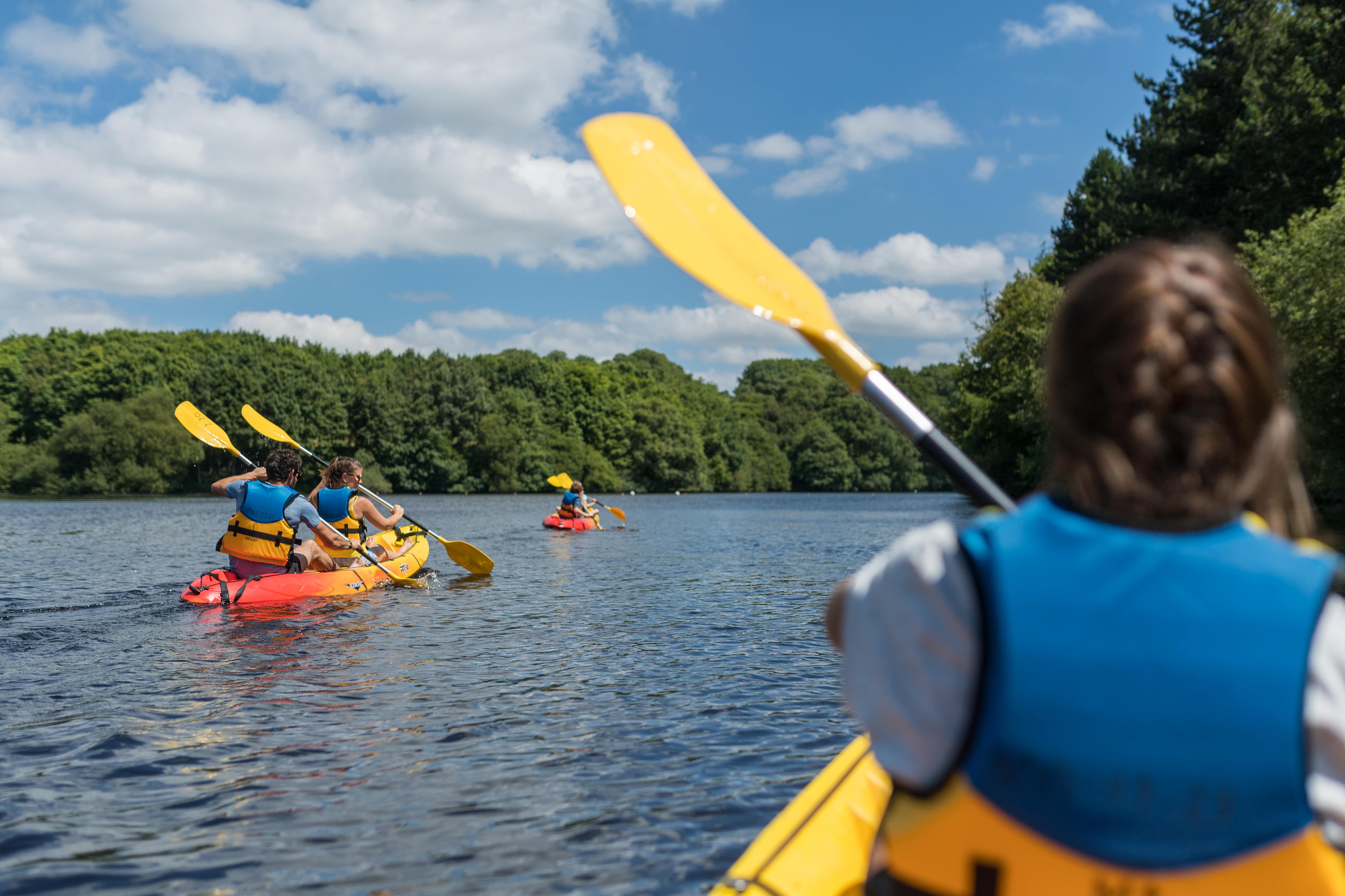 Vue sur une enfant, de dos, faisant du kayak ; autres personnes pagayant autour d'elle