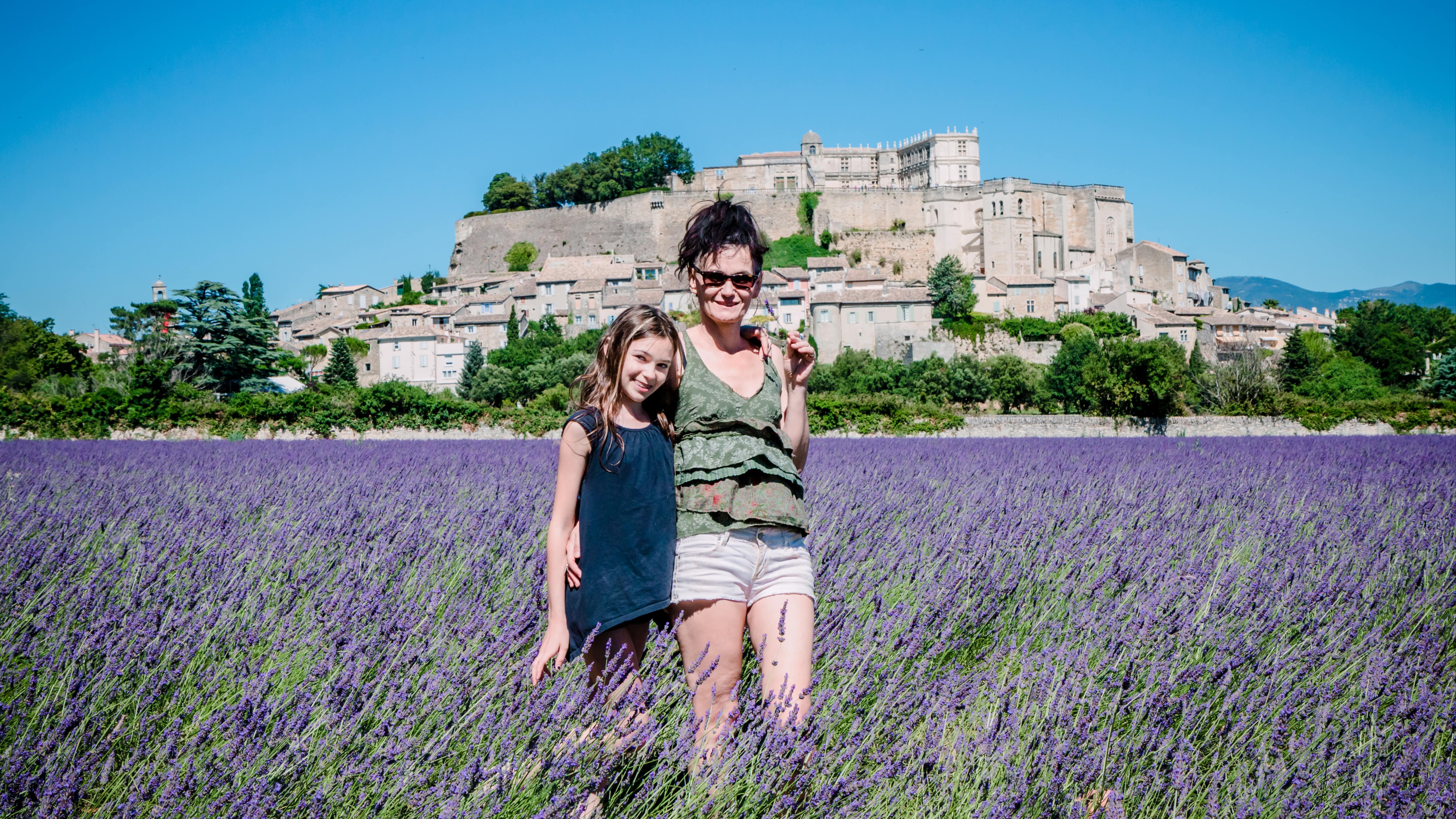 Femme et fillette dans un champ de lavande devant le village de Grignan et son château sur les hauteurs