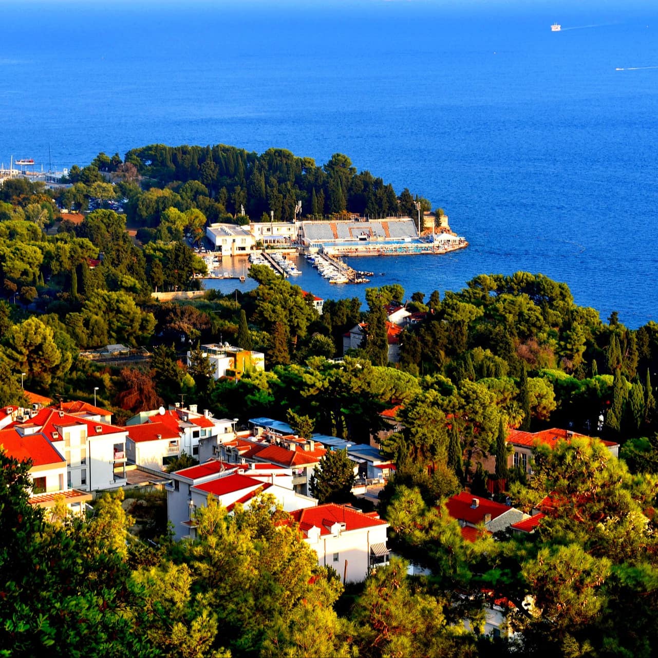 Croatian villas in the town of Split with lively red roofs, mature trees and the royal blue Adriatic Sea beyond