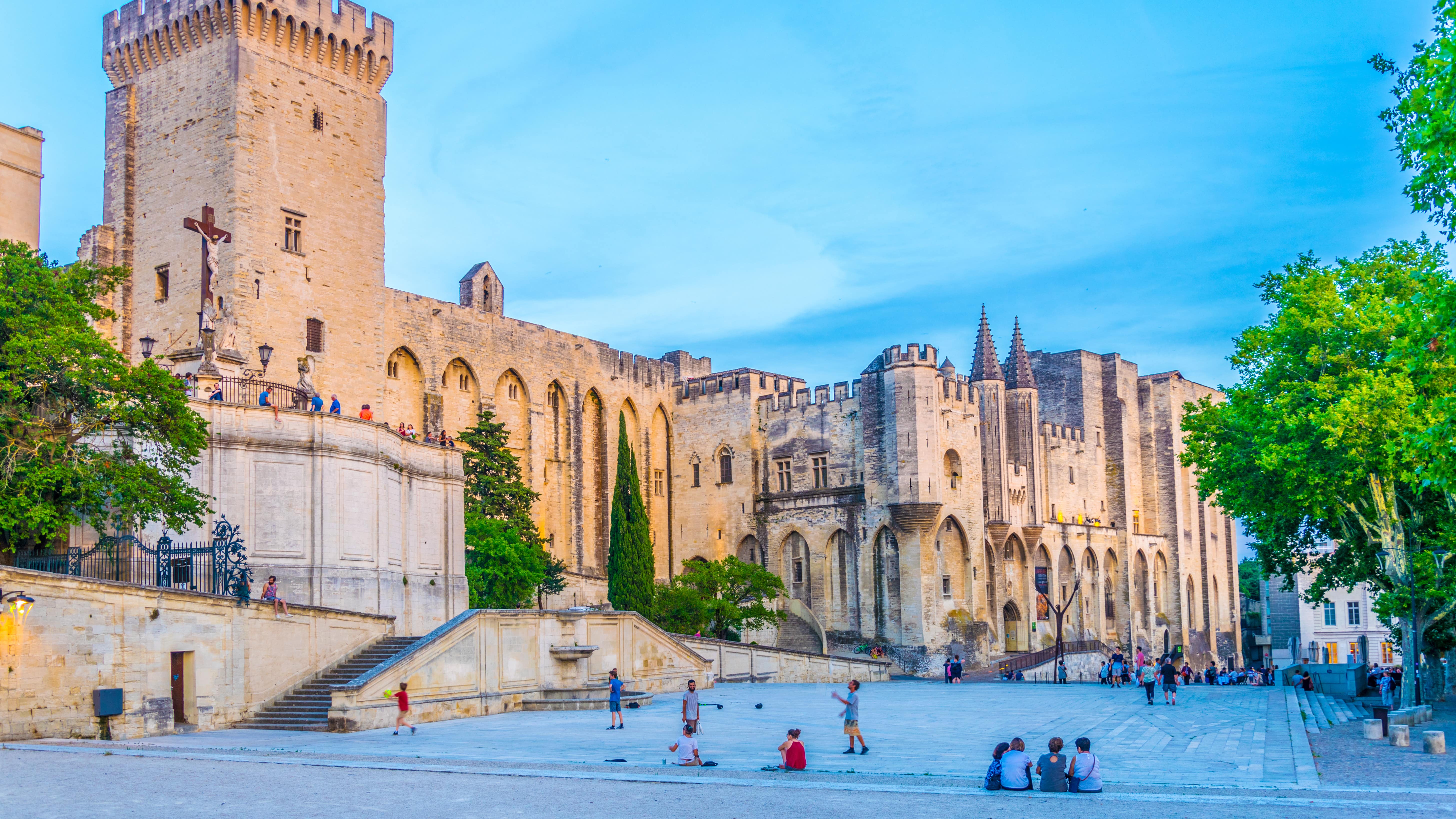 Différents groupes de personnes devant le Palais des Papes à Avignon lors d’un début de soirée d’été