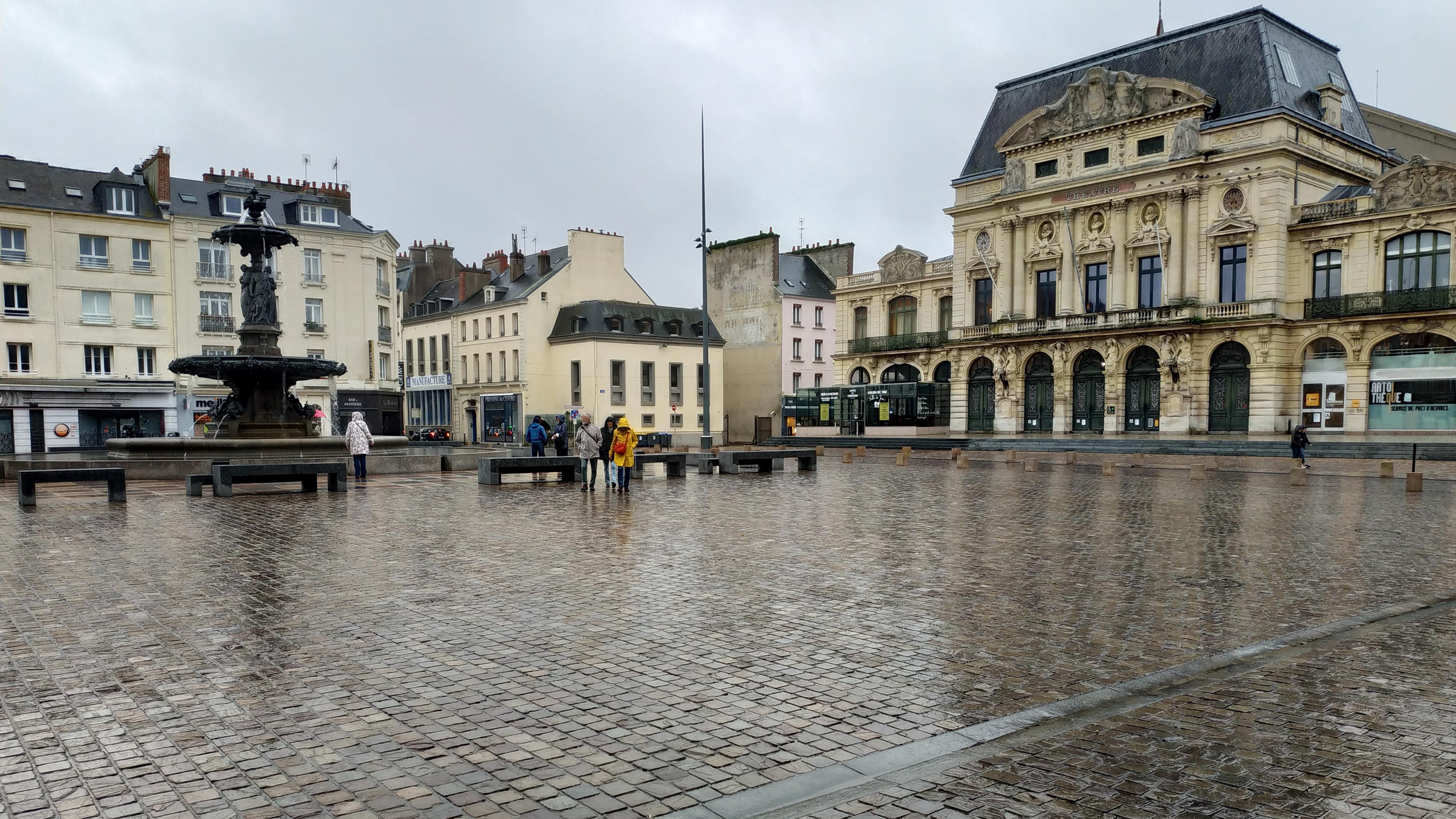 Place du Général-de-Gaulle, Cherbourg : place pavée avec fontaine et théâtre à l’italienne, un jour de pluie