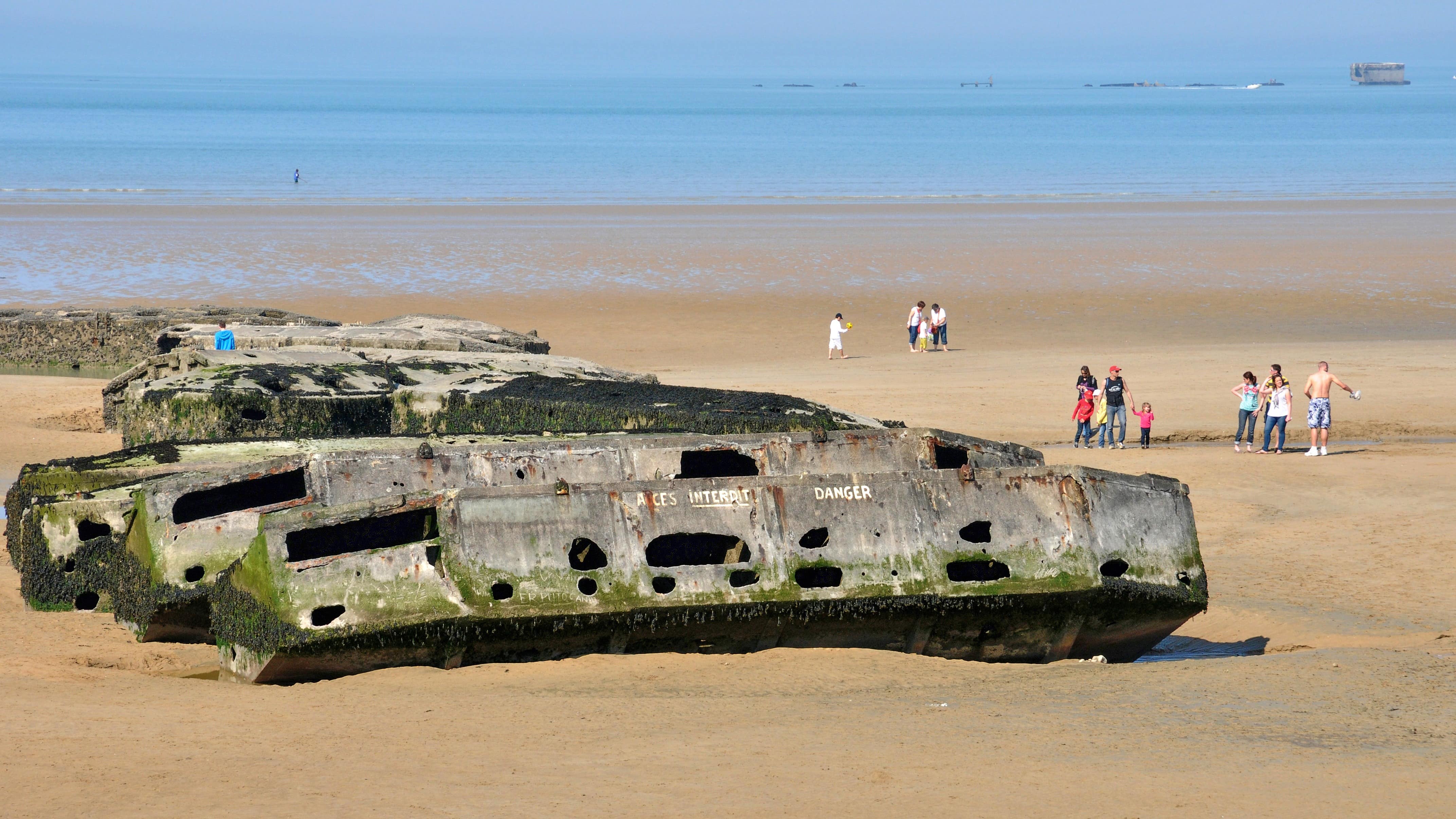 Des familles près des vestiges du port artificiel sur la plage d’Arromanches