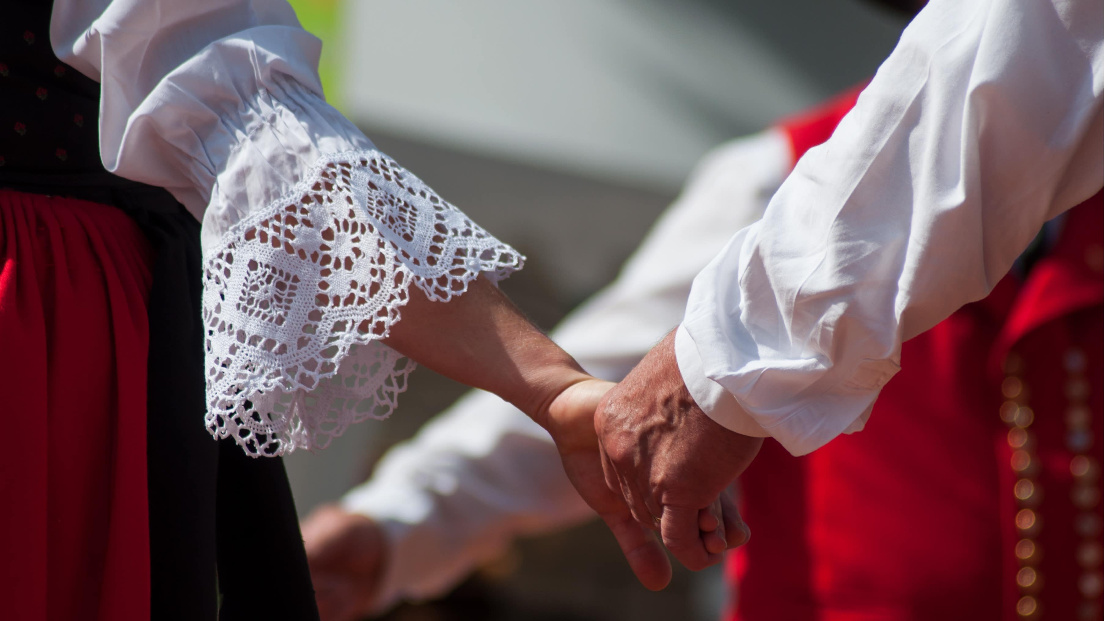 Gros plan sur deux personnes se donnant la main, elles portent un costume traditionnel alsacien