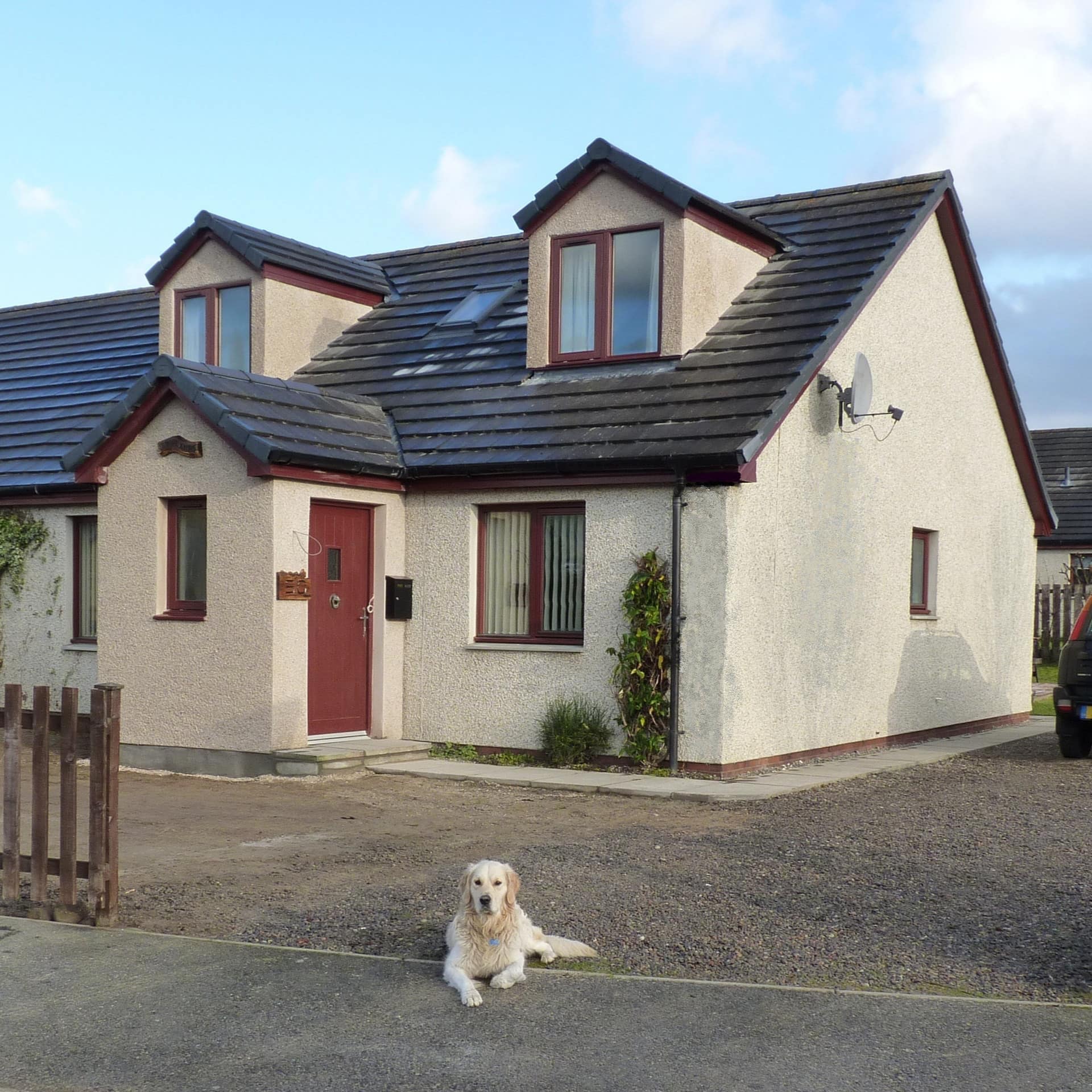 A furry white dog sitting in front of a modern cottage rental