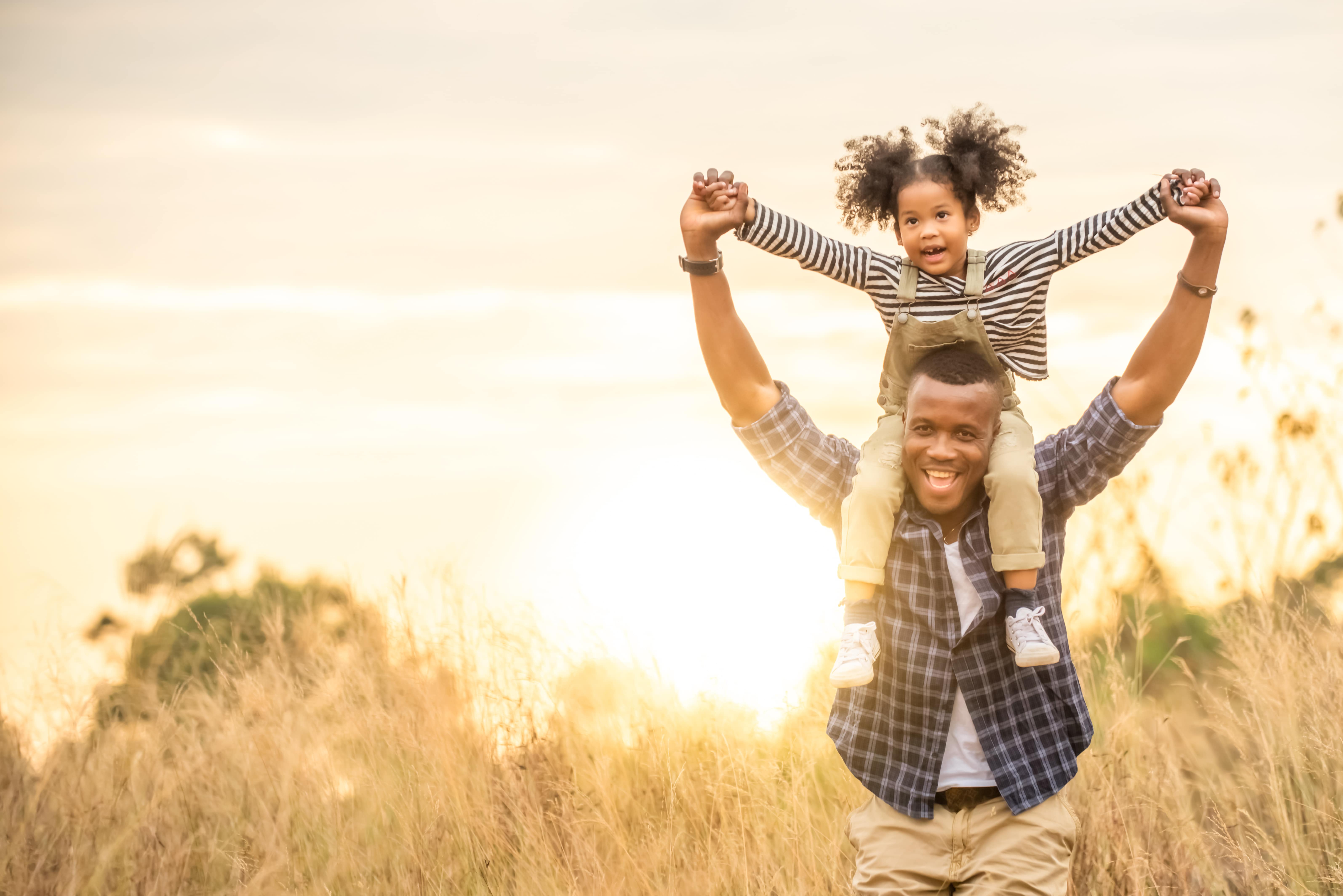 fille assise sur les épaules de son père alors qu'il traverse un champ