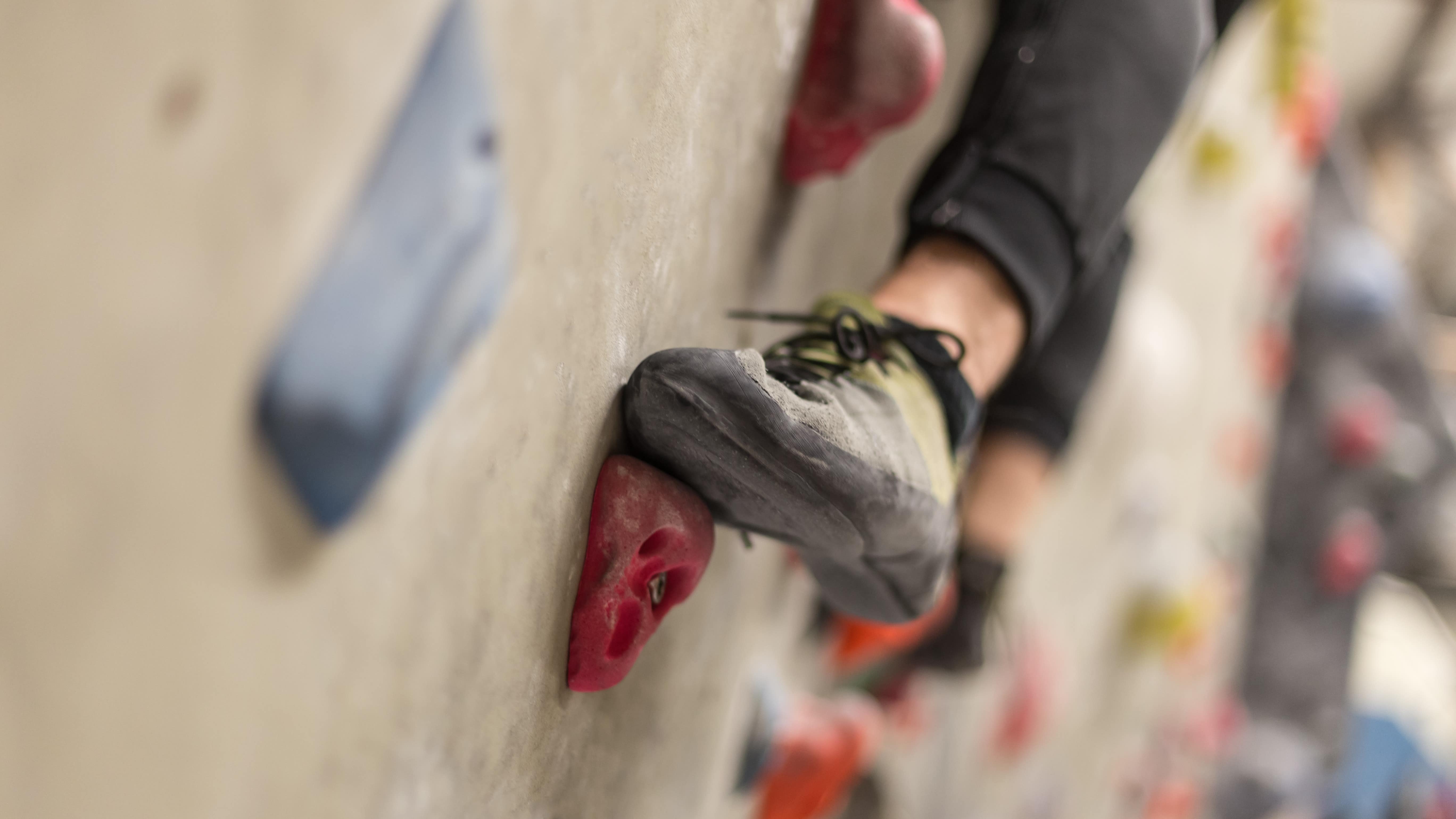 Gros plan sur quelques prises d'un mur d'escalade, ainsi que sur les pieds de quelqu'un en train de grimper