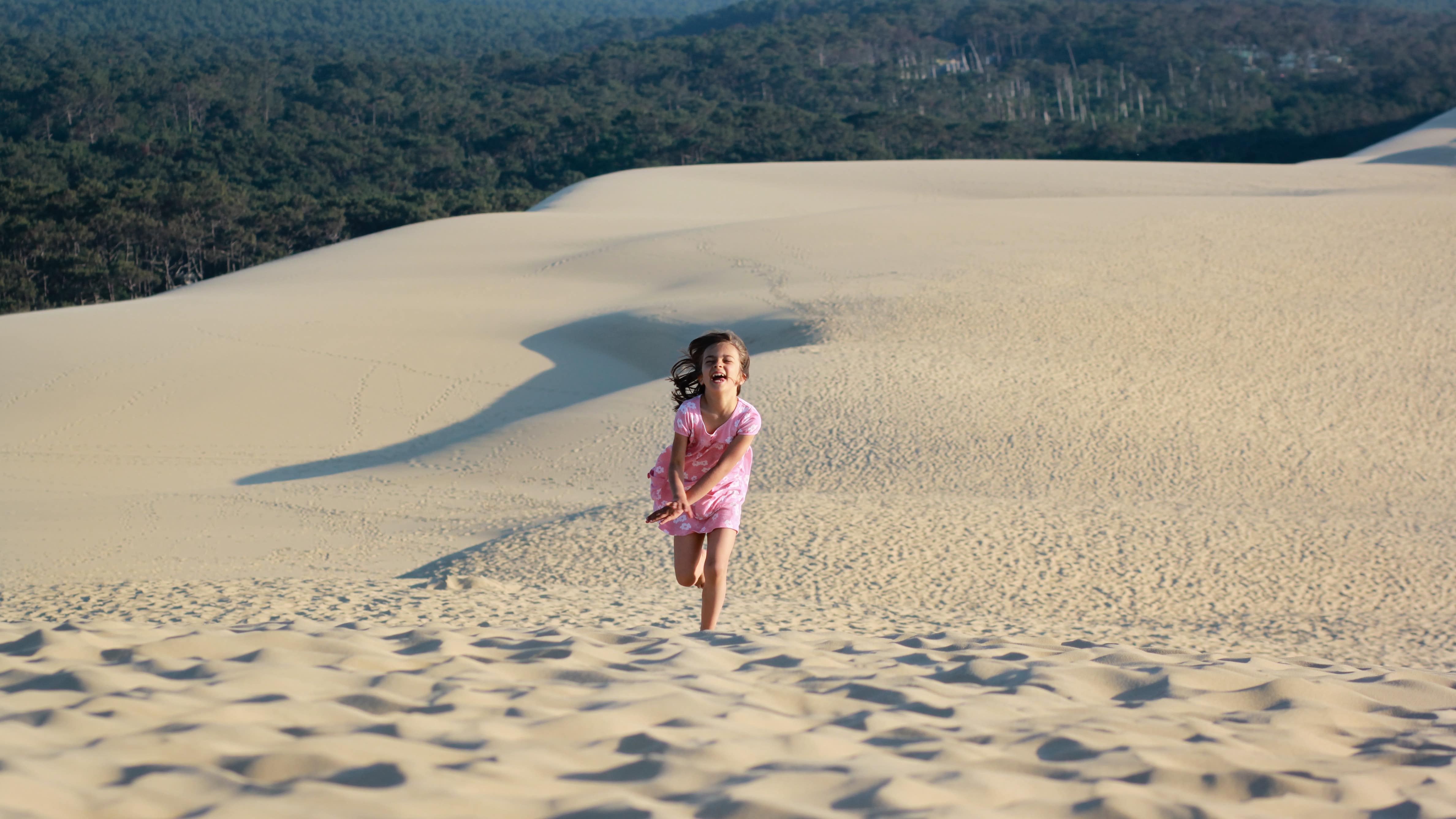 Fillette courant sur le sable de la dune du Pilat, avec la forêt en arrière-plan