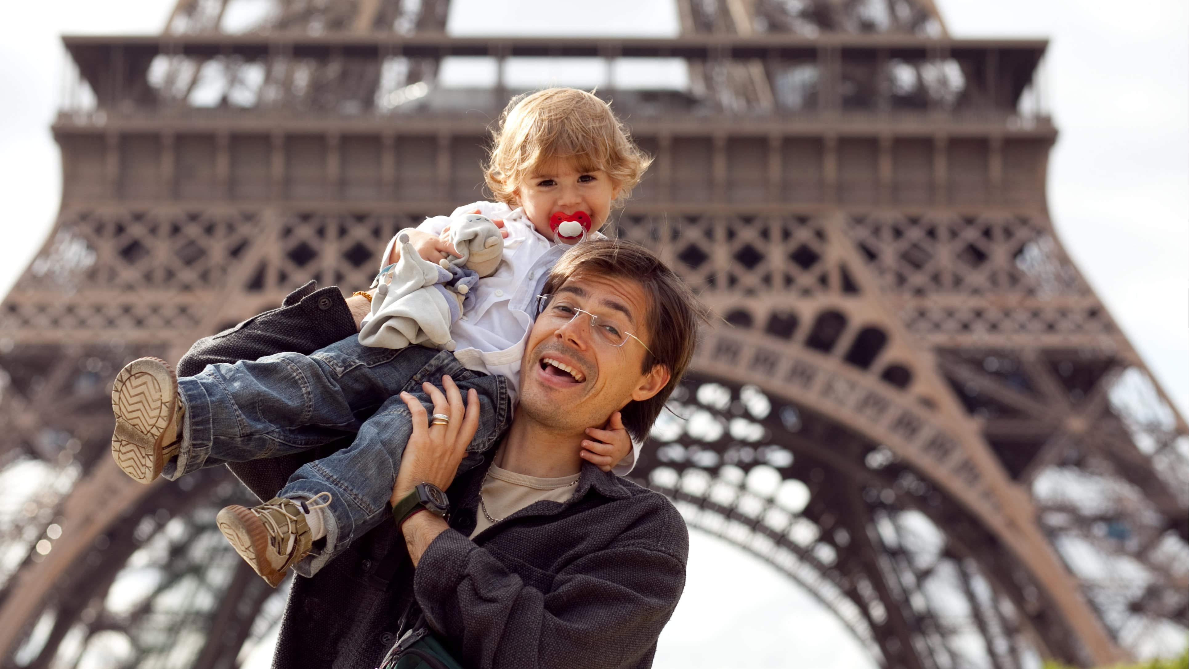Un père tenant son bébé sur l’épaule avec la tour Eiffel derrière eux