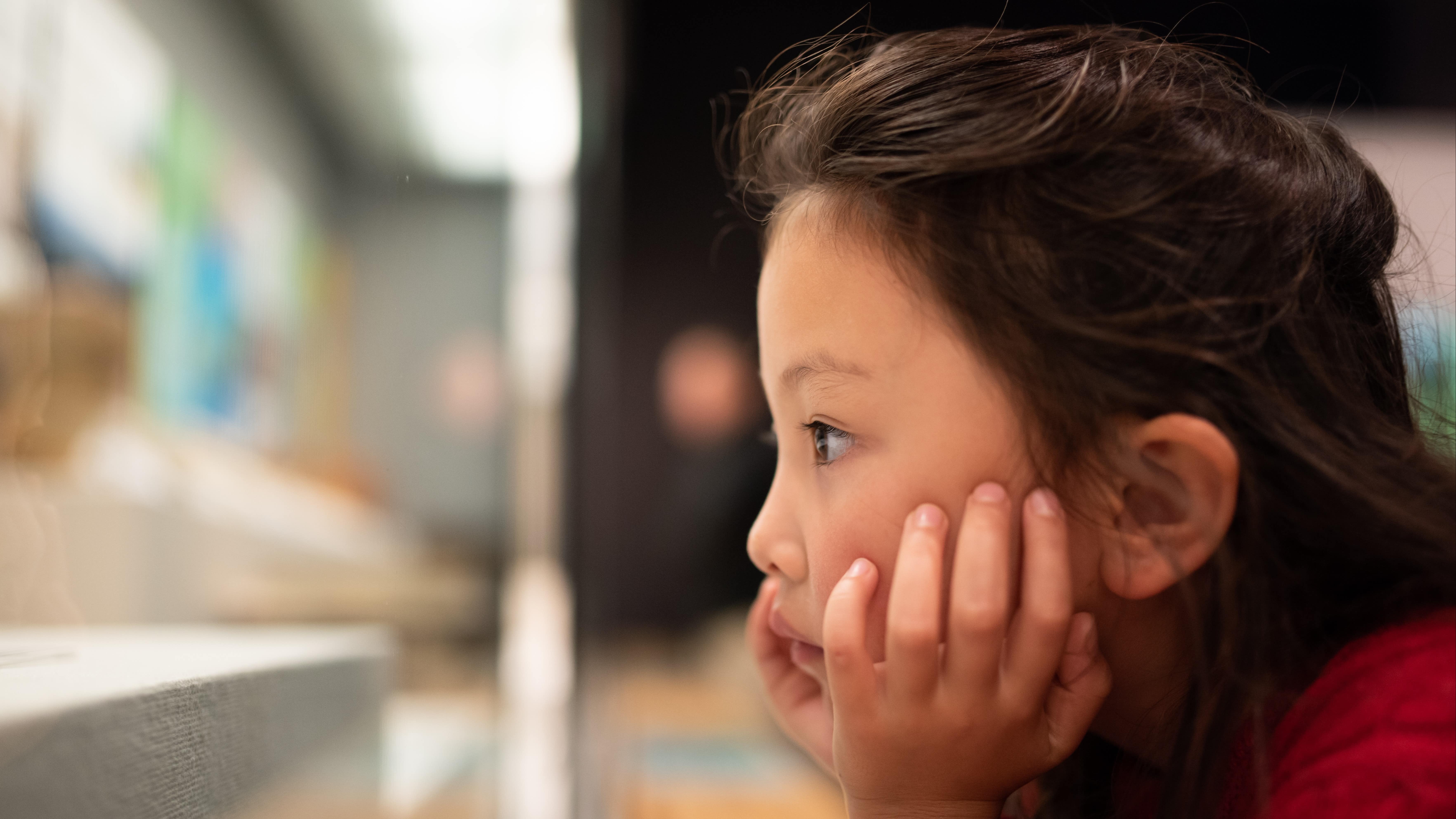 Petite fille rêveuse devant une vitrine, dans un musée