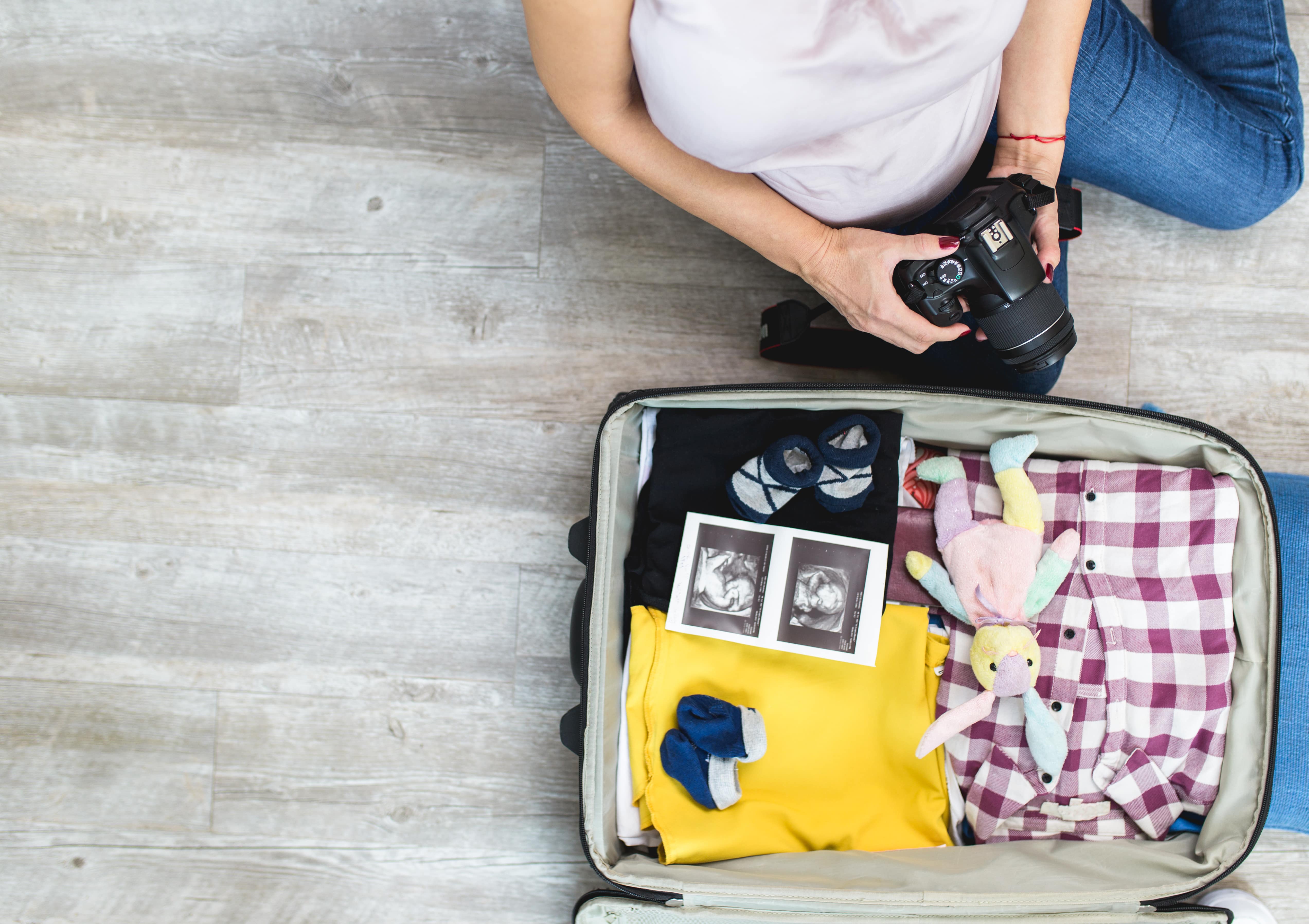 Femme enceinte à côté d'ouvrir le sac du voyageur avec échographie de son bébé, chaussettes de bébé, vêtements et appareil photo. Concept de voyage et de vacances.