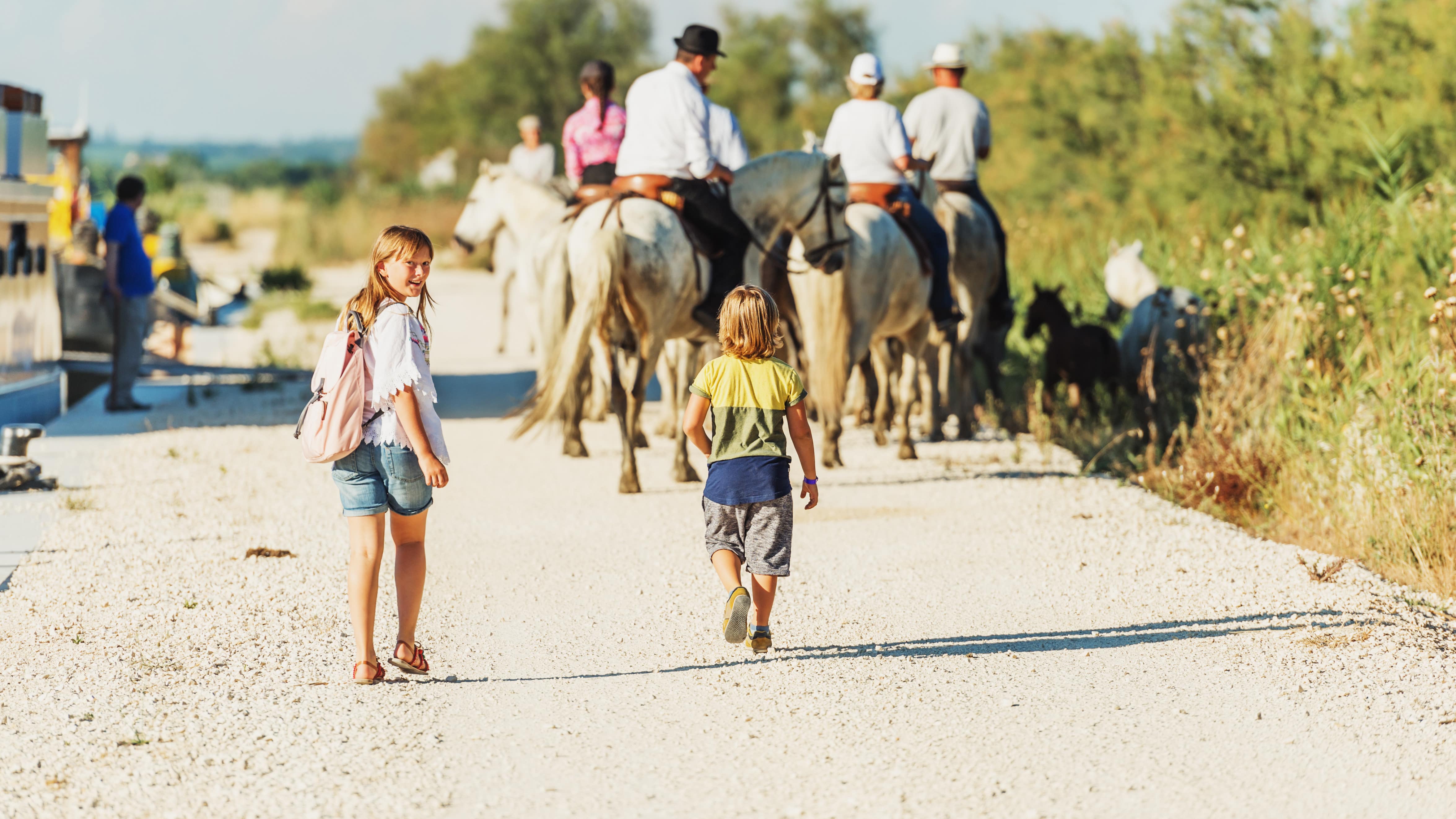 Deux enfants marchant sur un chemin derrière un groupe de personnes sur des chevaux blancs dans le Parc naturel de Camargue