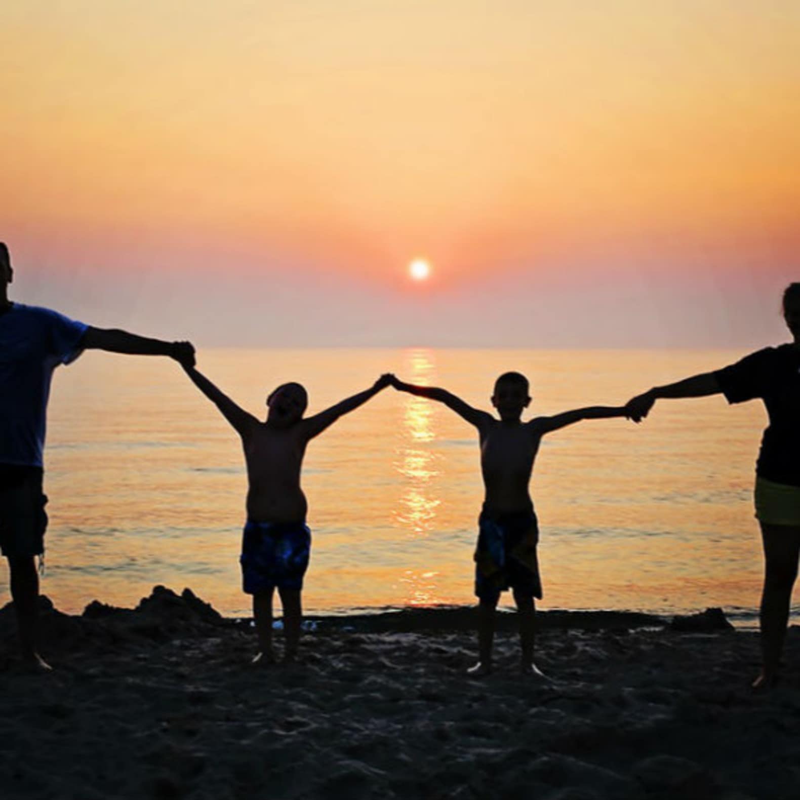 Famille avec deux enfants se tenant la main, sur la plage au soleil couchant, location Marseillan plage