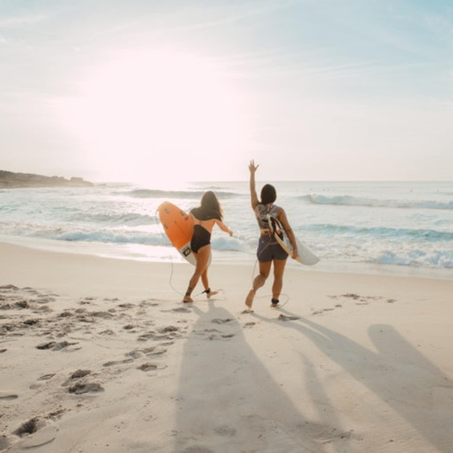 Deux femmes sur la plage avec une planche de surf, face à la mer