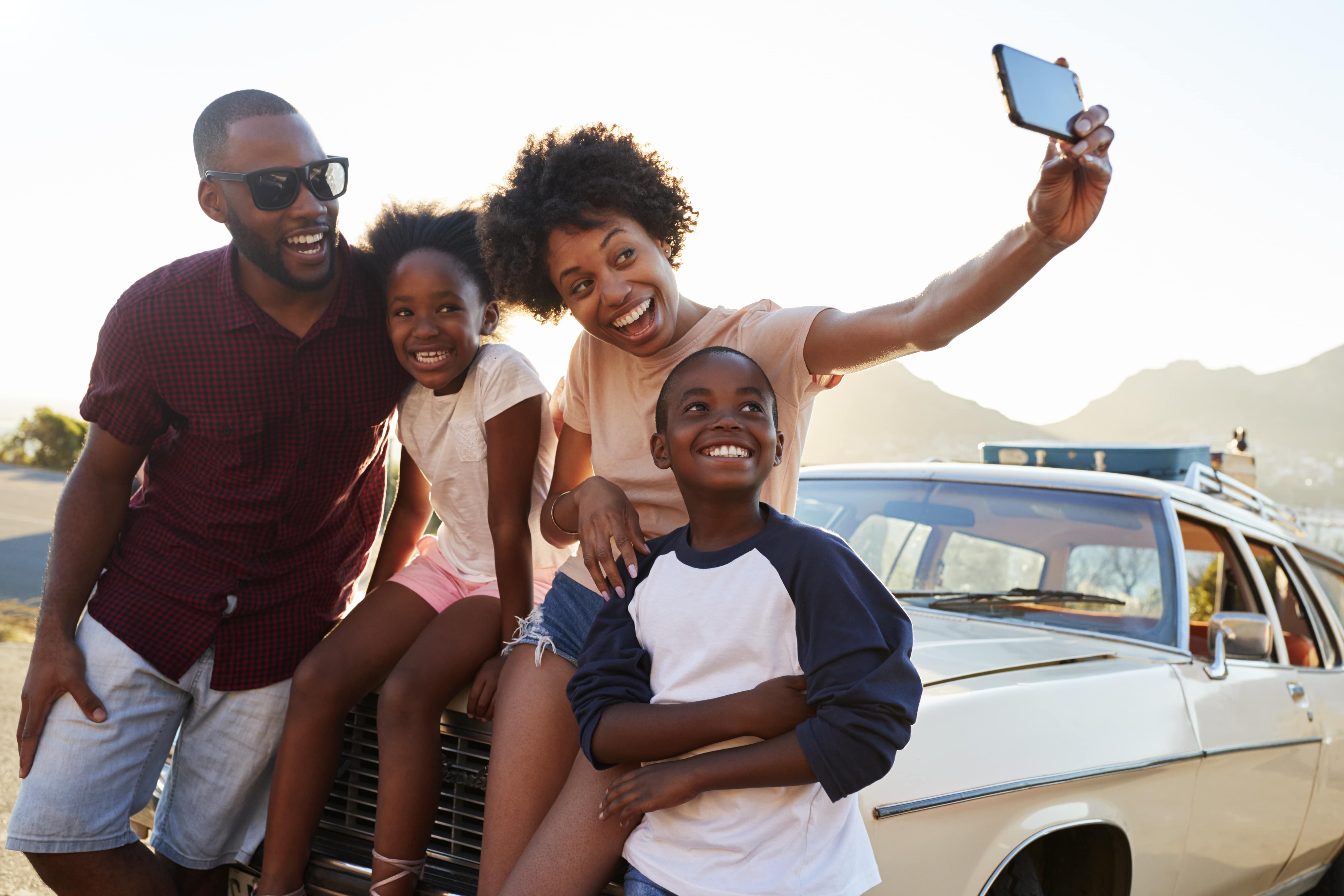 Selfie familial à côté de la voiture emballée pour un voyage en voiture